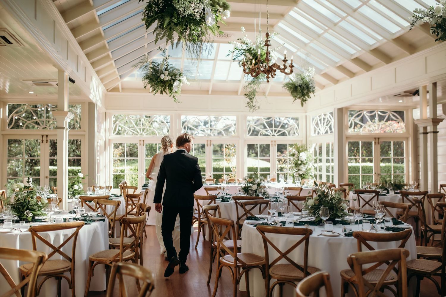 Elegant wedding reception venue with glass ceiling and wooden cross-back chairs.