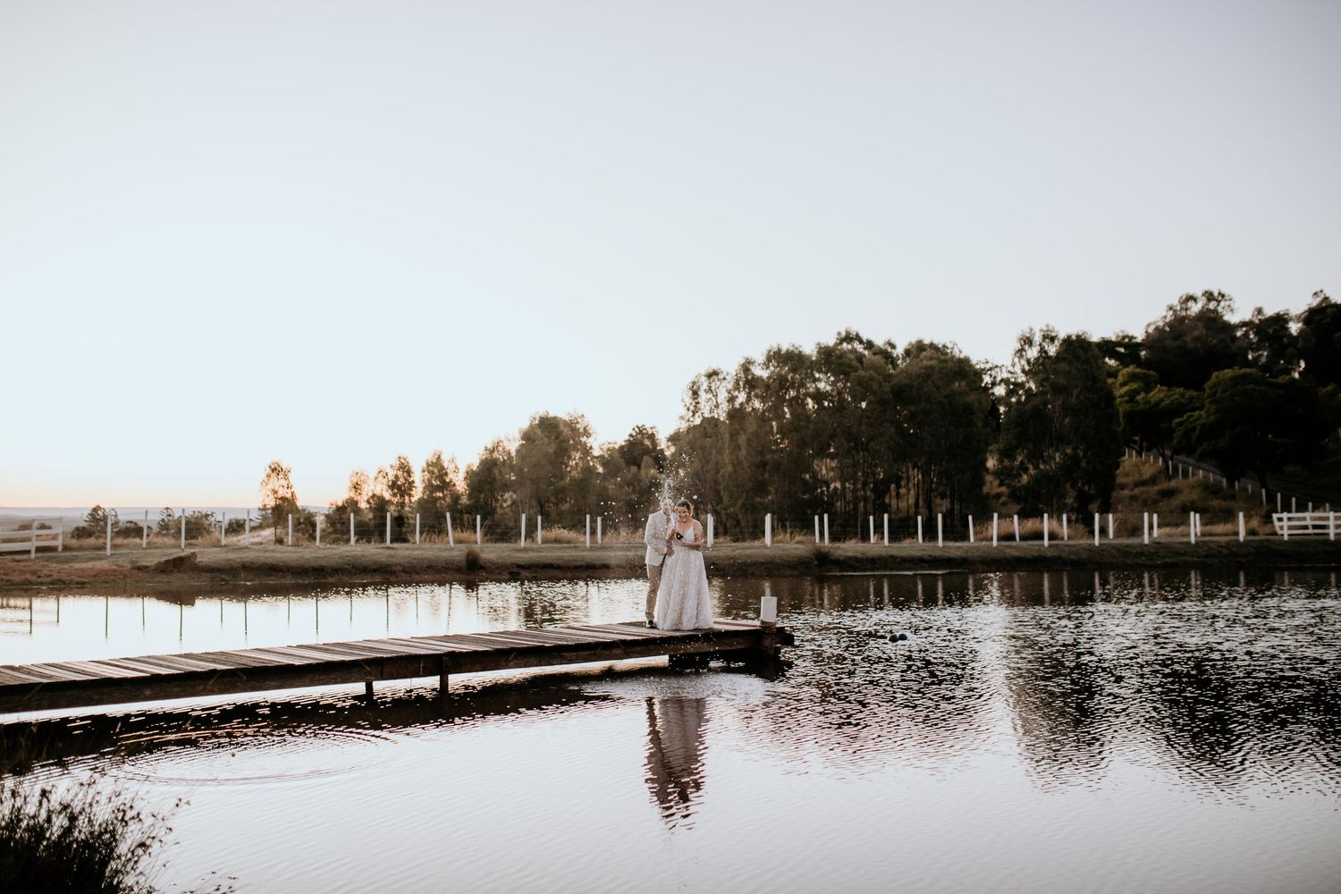 Serene lakeside scene with a wooden dock stretching into calm waters at sunset.