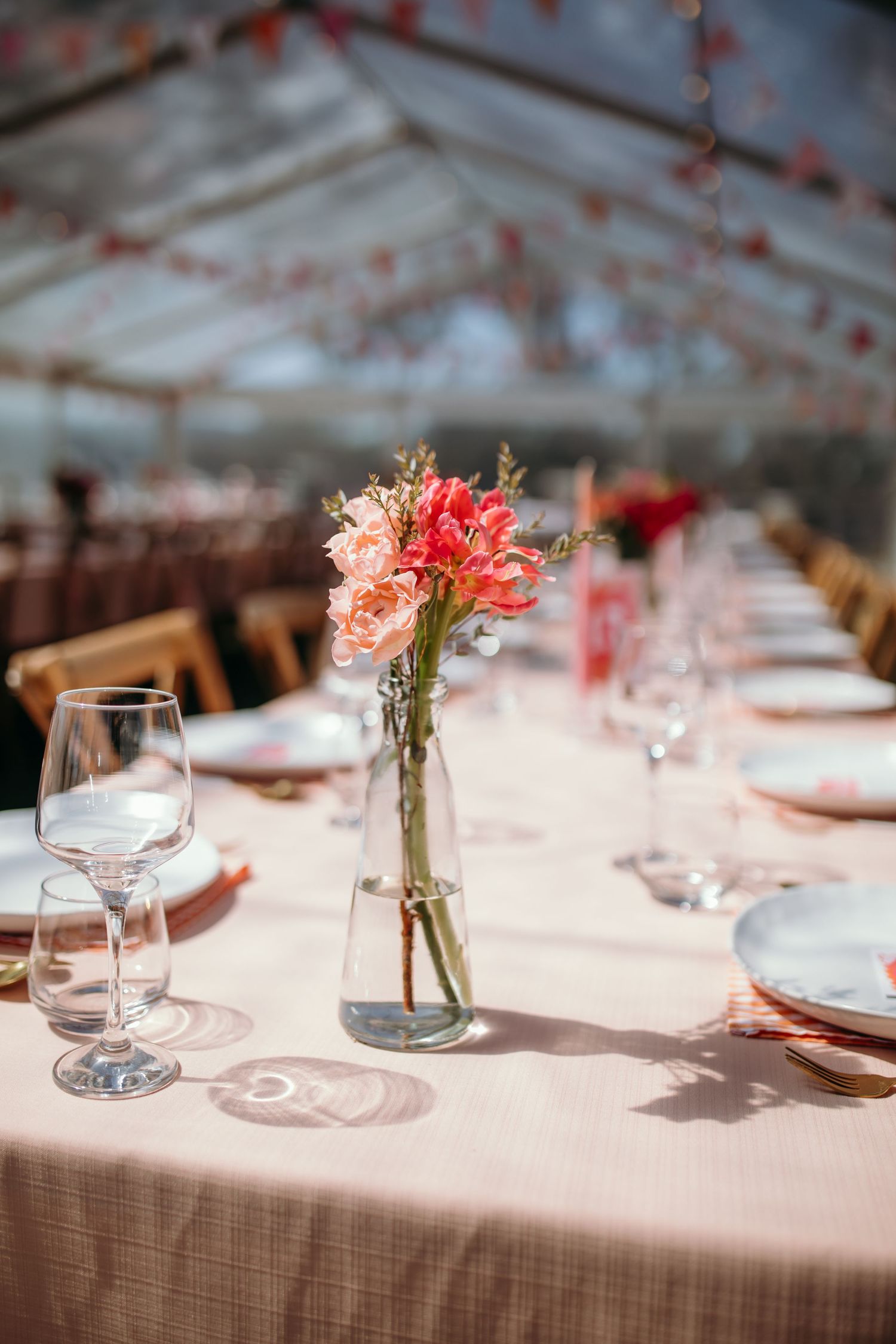 Elegant table settings with coral floral centerpieces in glass vases at wedding reception.