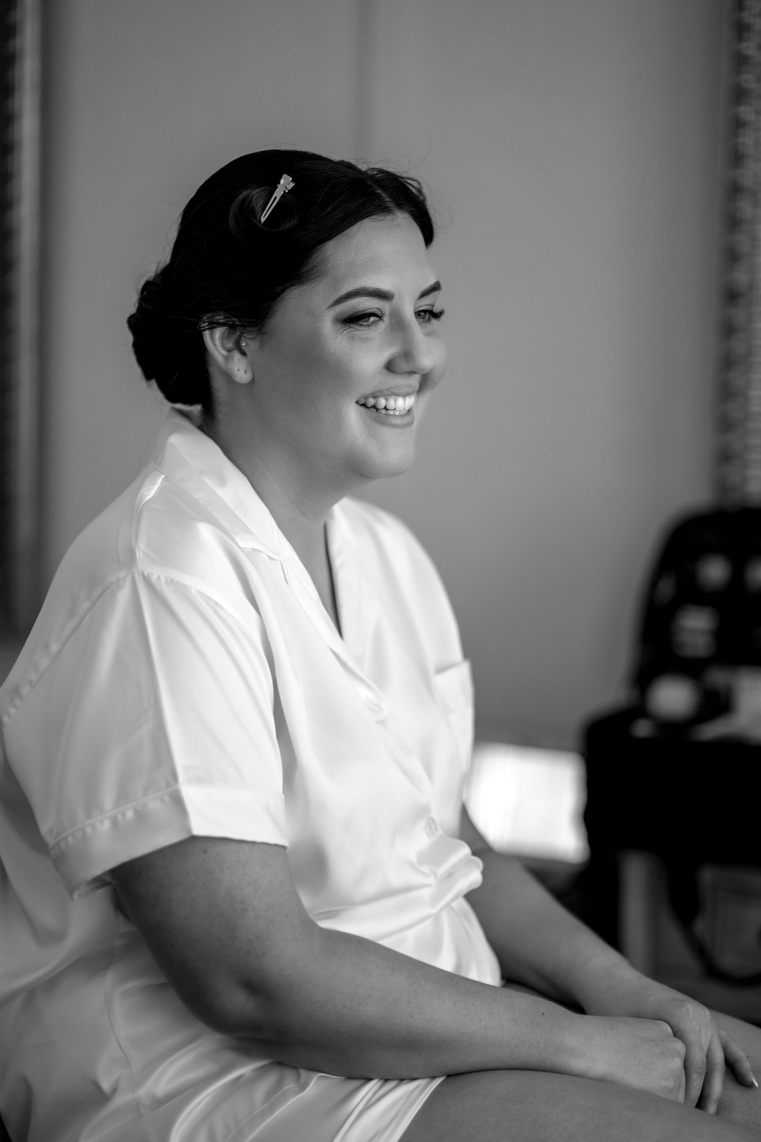 A candid black and white photo shows someone in a white shirt smiling while seated indoors.