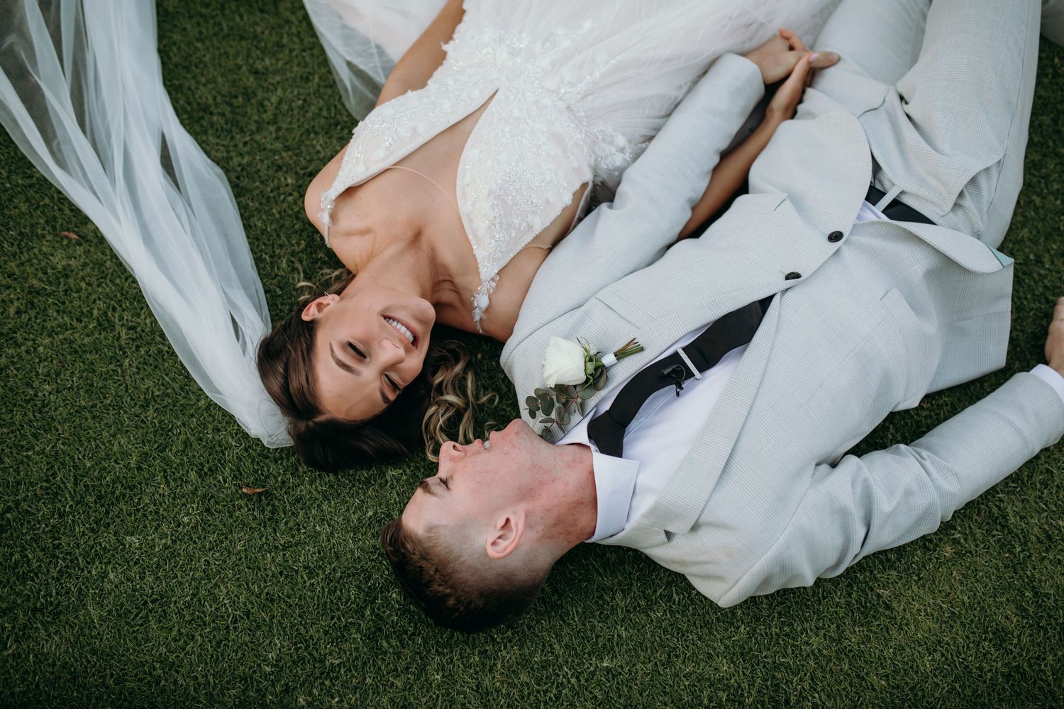 Newlyweds lay on grass sharing romantic moments during outdoor photo session.
