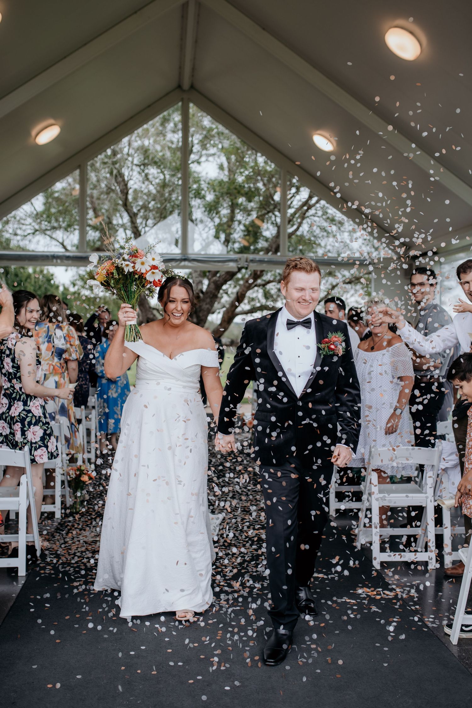 Wedding ceremony exit with confetti shower under a modern white tent structure.