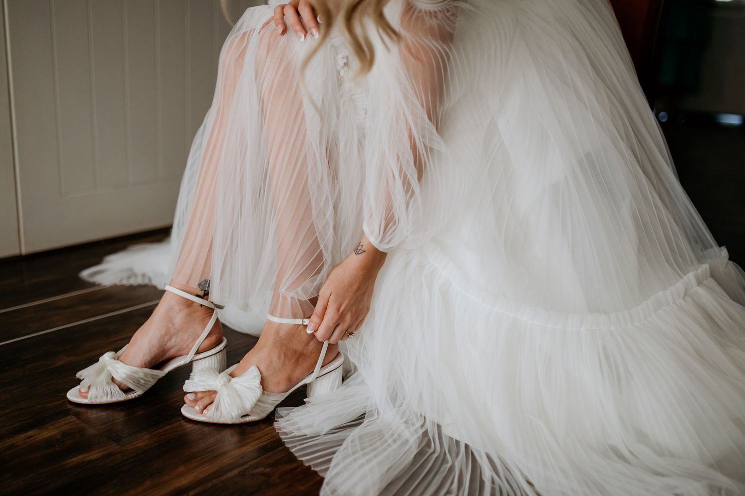 Elegant bridal shoes and wedding dress details captured in soft, natural light.