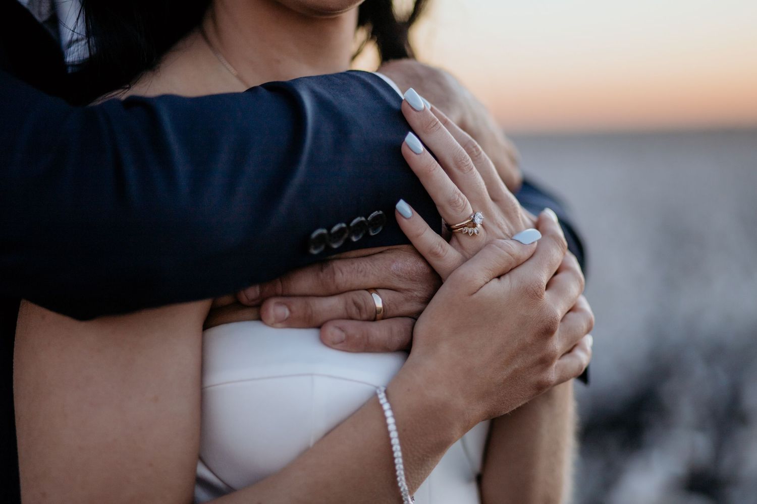 Close-up shot of hands holding each other tenderly during an intimate wedding moment at sunset.