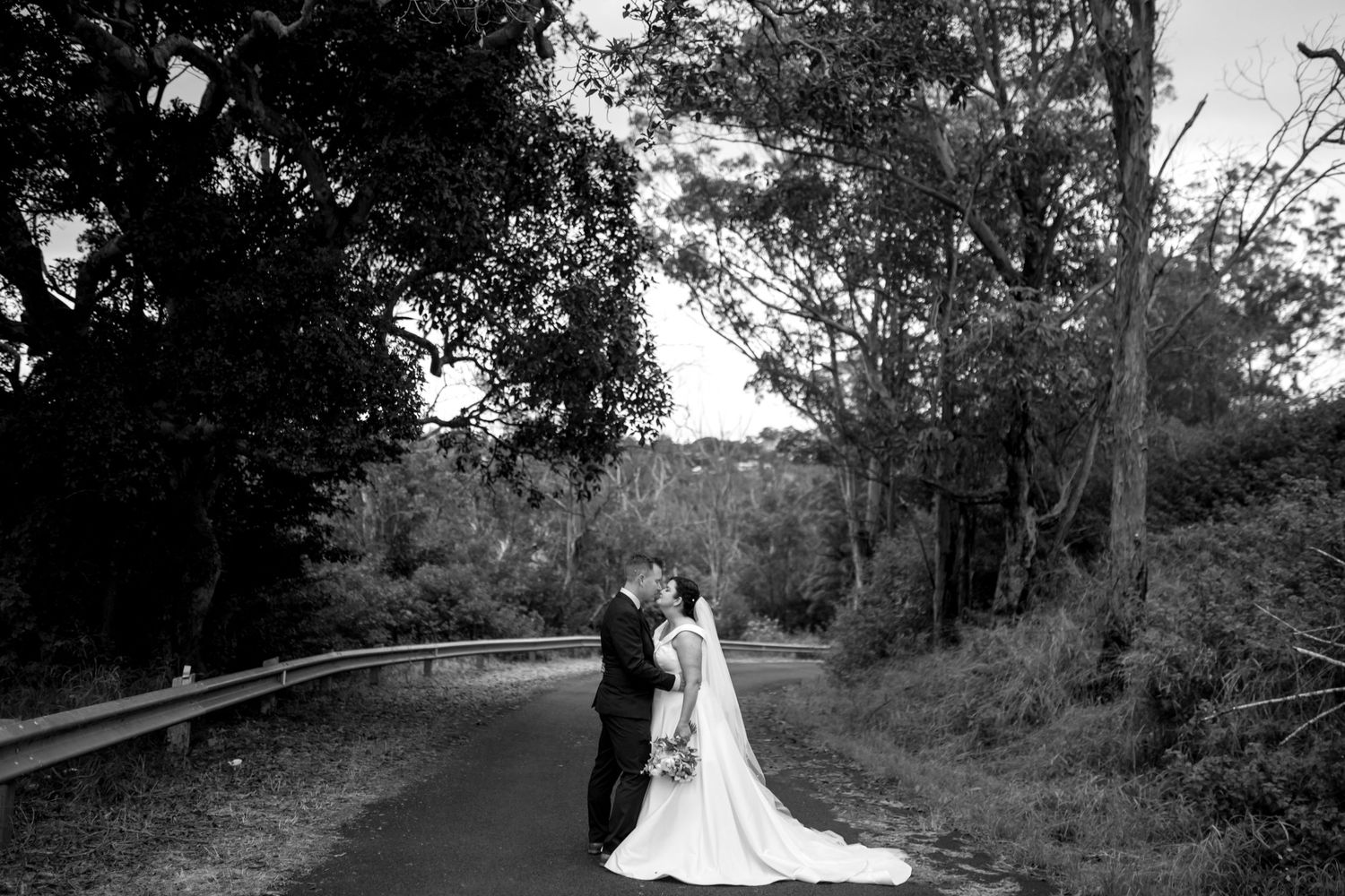 Wedding couple walking along a tree-lined path at sunset.