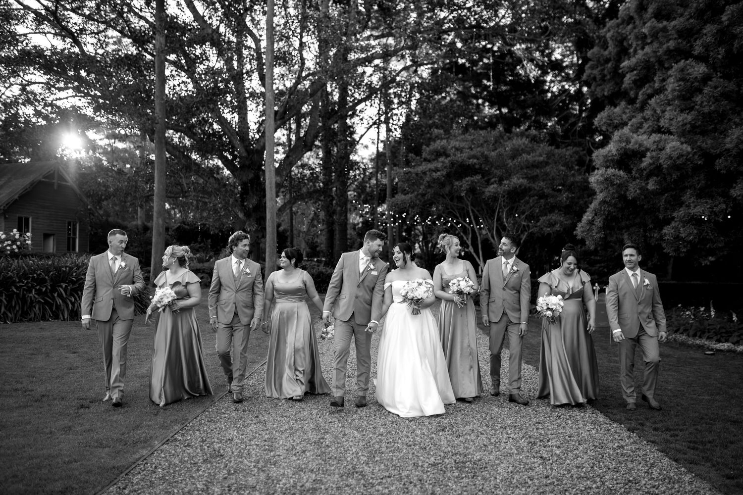 Wedding party poses outdoors in a garden setting with trees and natural greenery.