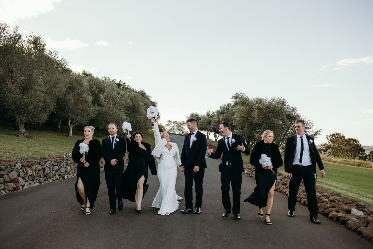 Wedding party walks together in a line across a grassy hillside during sunset.