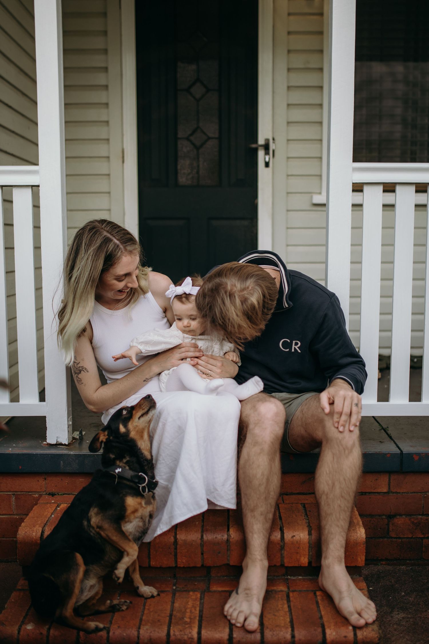 Family sitting on front porch steps with dog while sharing intimate moment with baby.