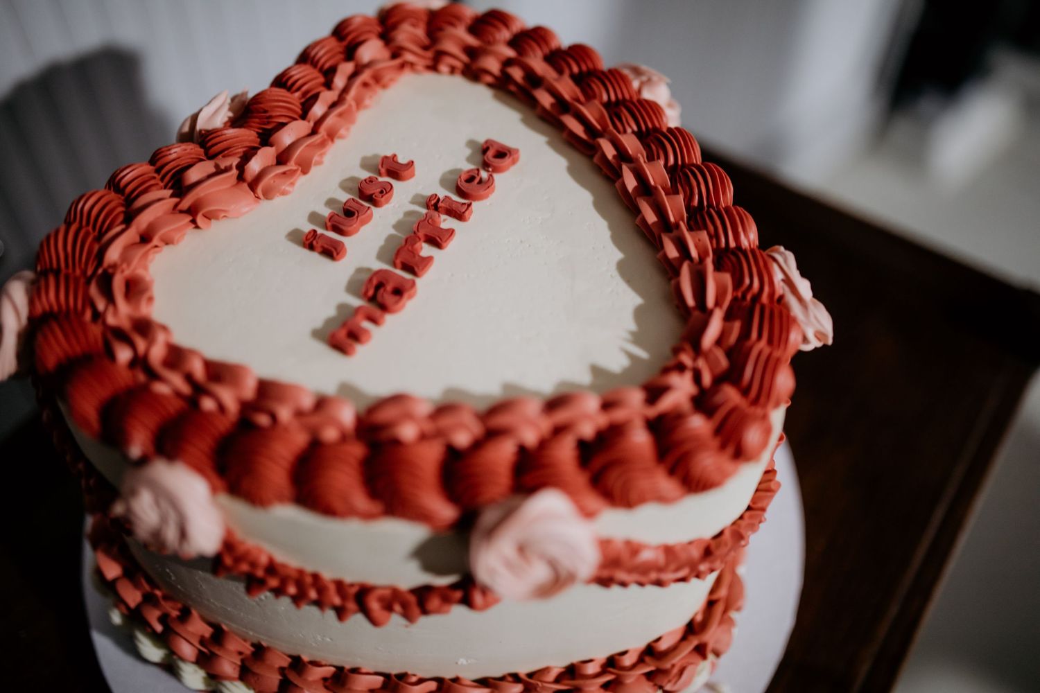 A red and white decorated wedding cake with delicate piping details and ruffled frosting tiers.