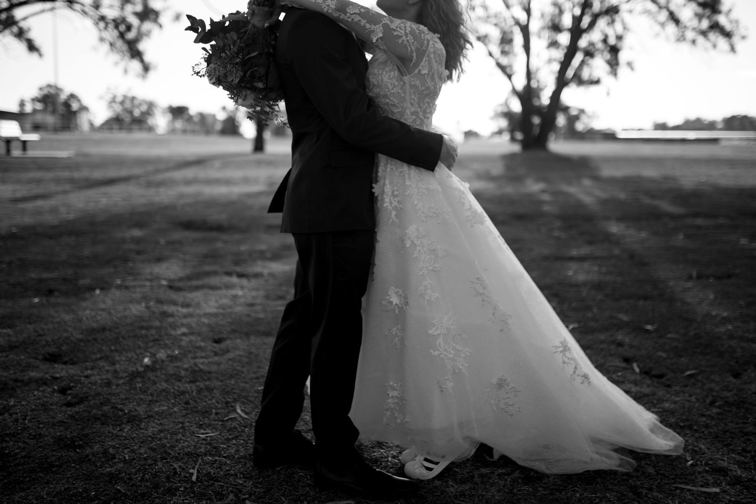 Silhouetted wedding couple embracing on an outdoor path at dusk.