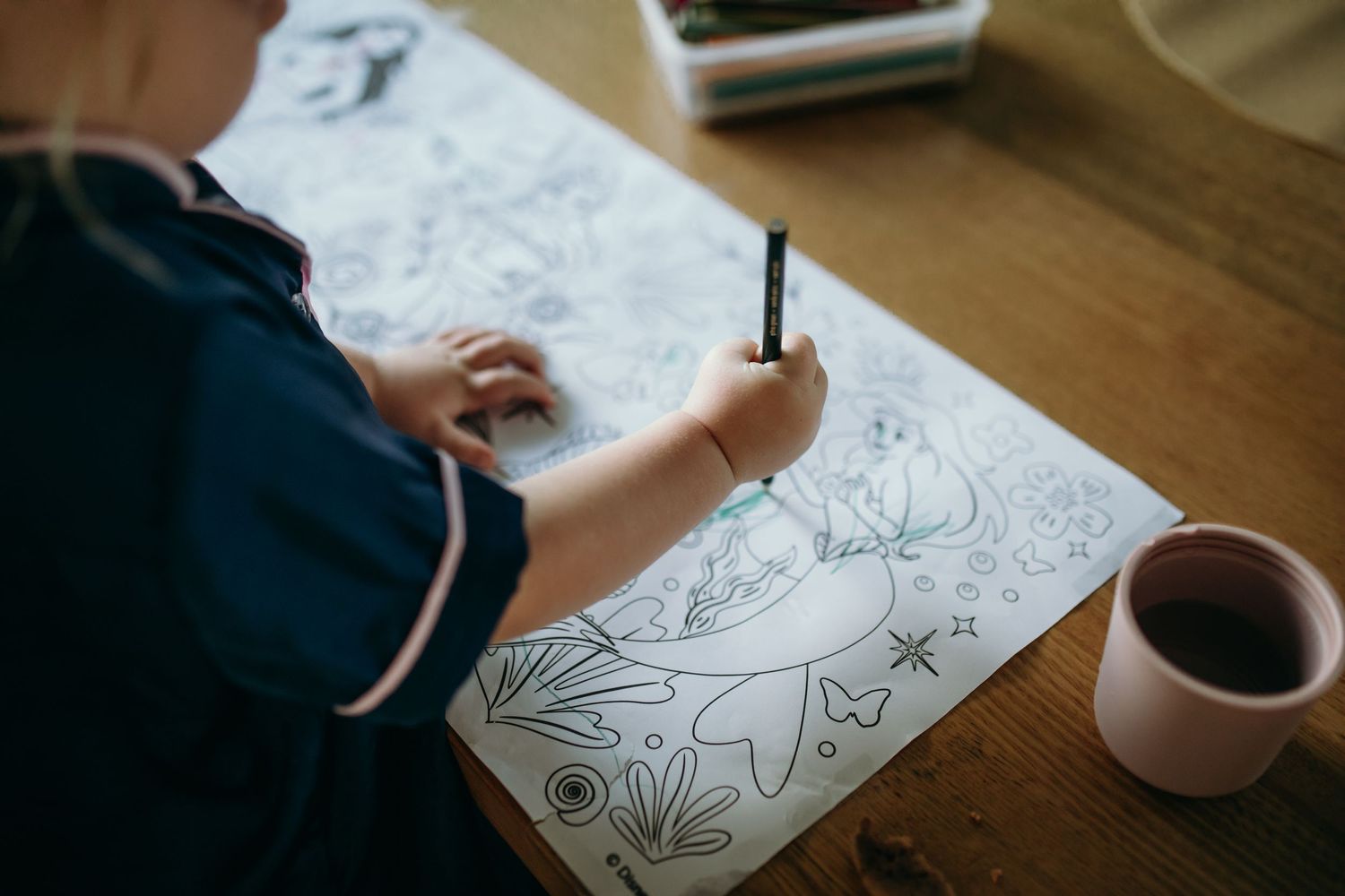 Close-up view of hands drawing and coloring on white paper with artistic designs.