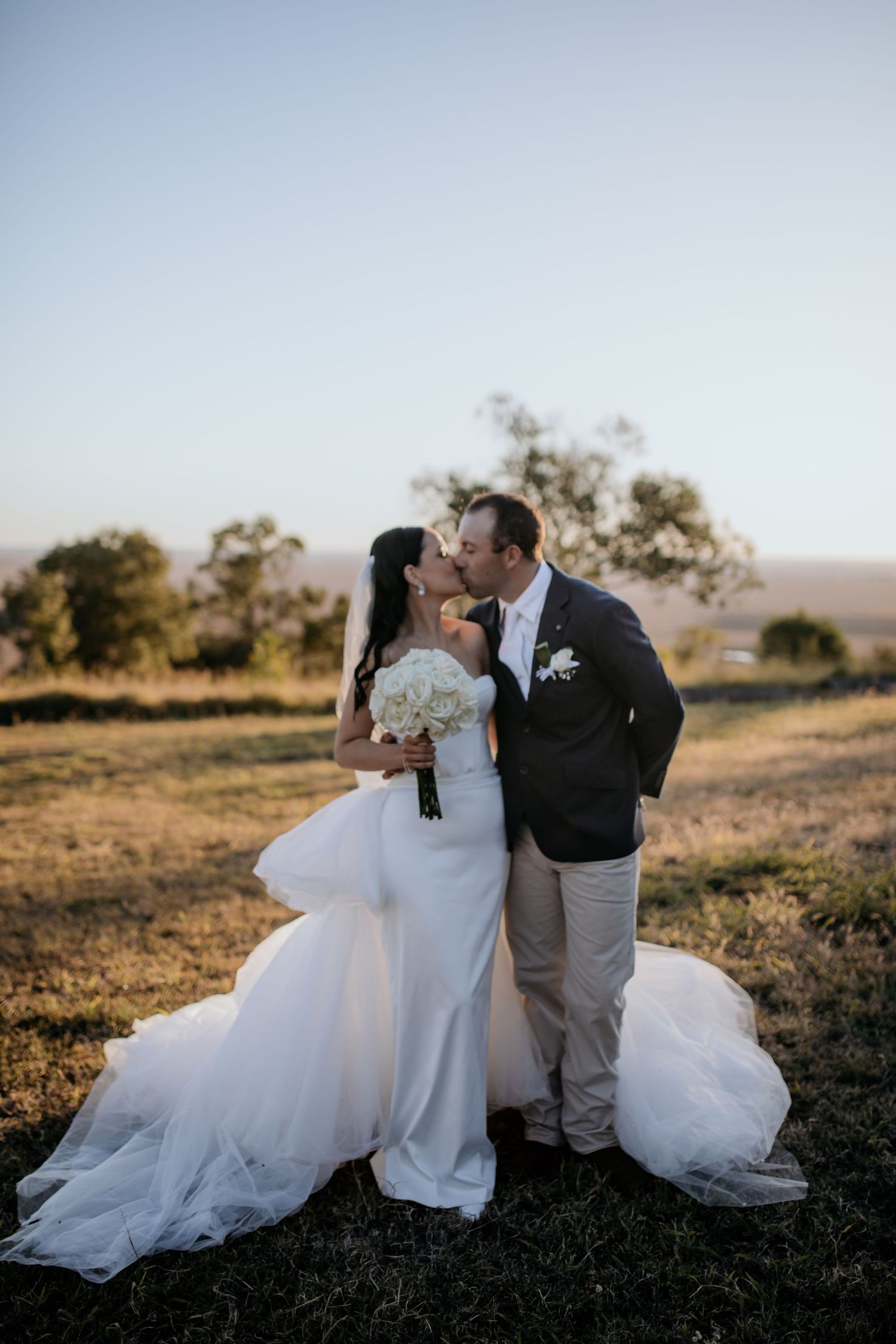 Romantic sunset portrait of newlyweds in an open field with flowing white wedding dress.