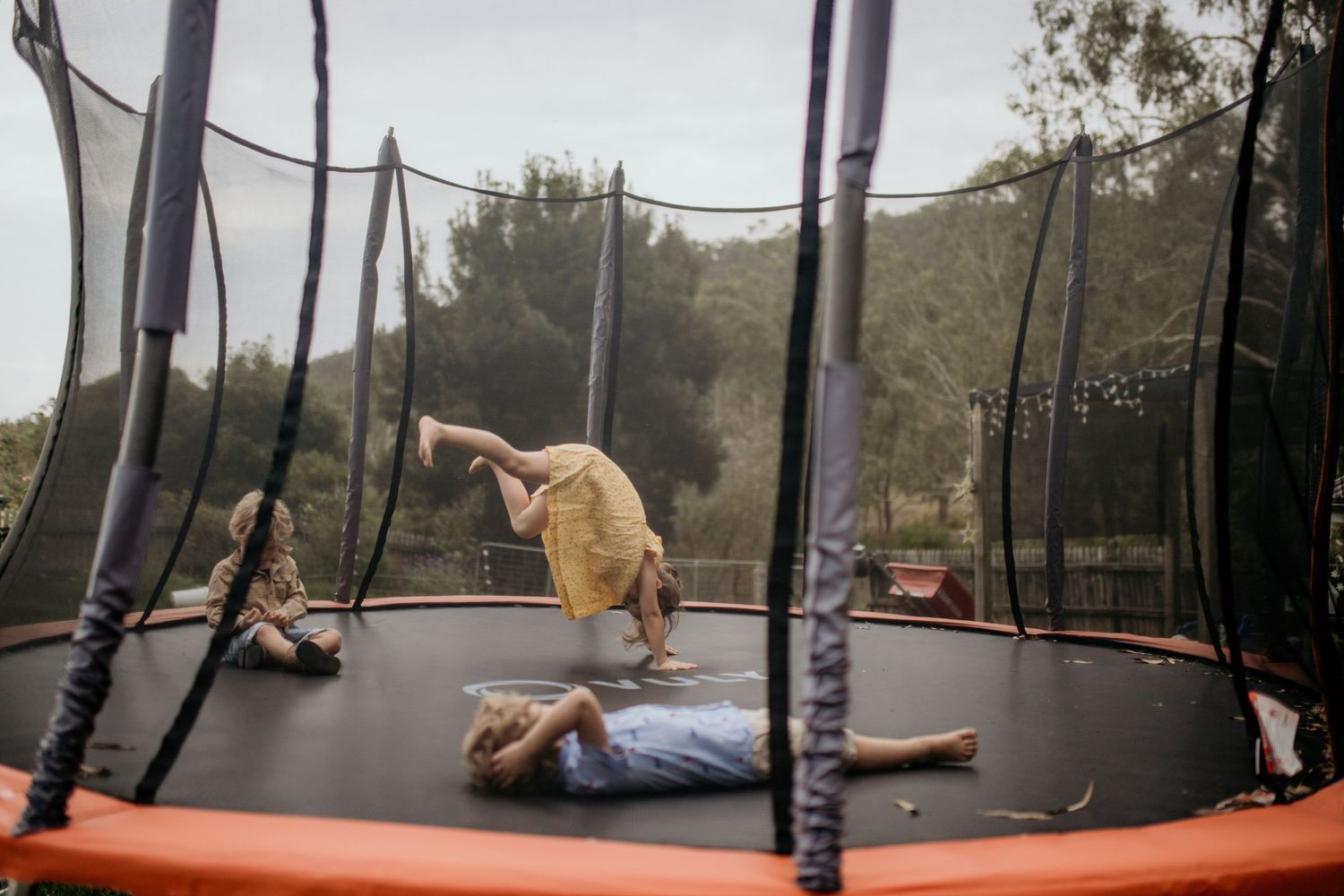 Children playing and jumping on a large outdoor trampoline with safety netting during a golden afternoon.