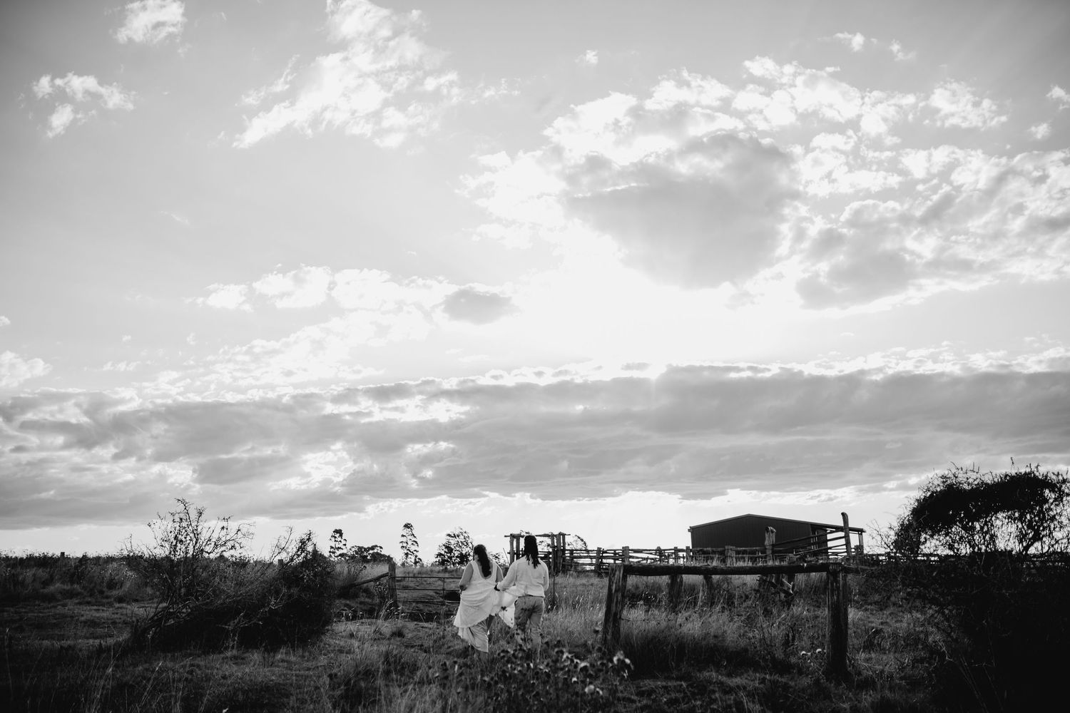 Panoramic black and white landscape view of rolling hills and scattered buildings under dramatic cloudy skies.