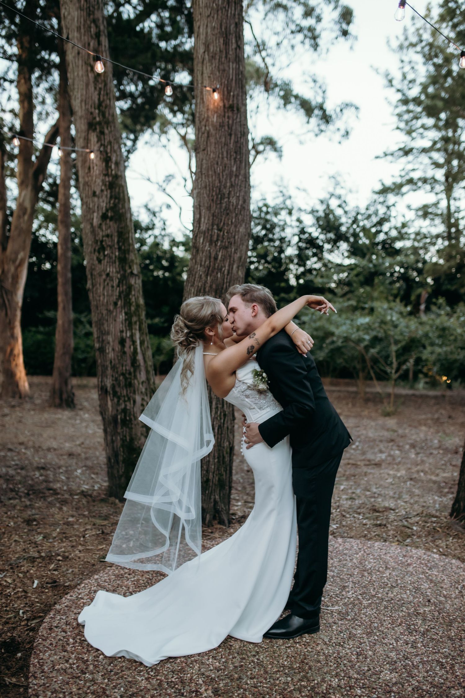 Romantic dance sequence between newlyweds on a tree-lined path at dusk.