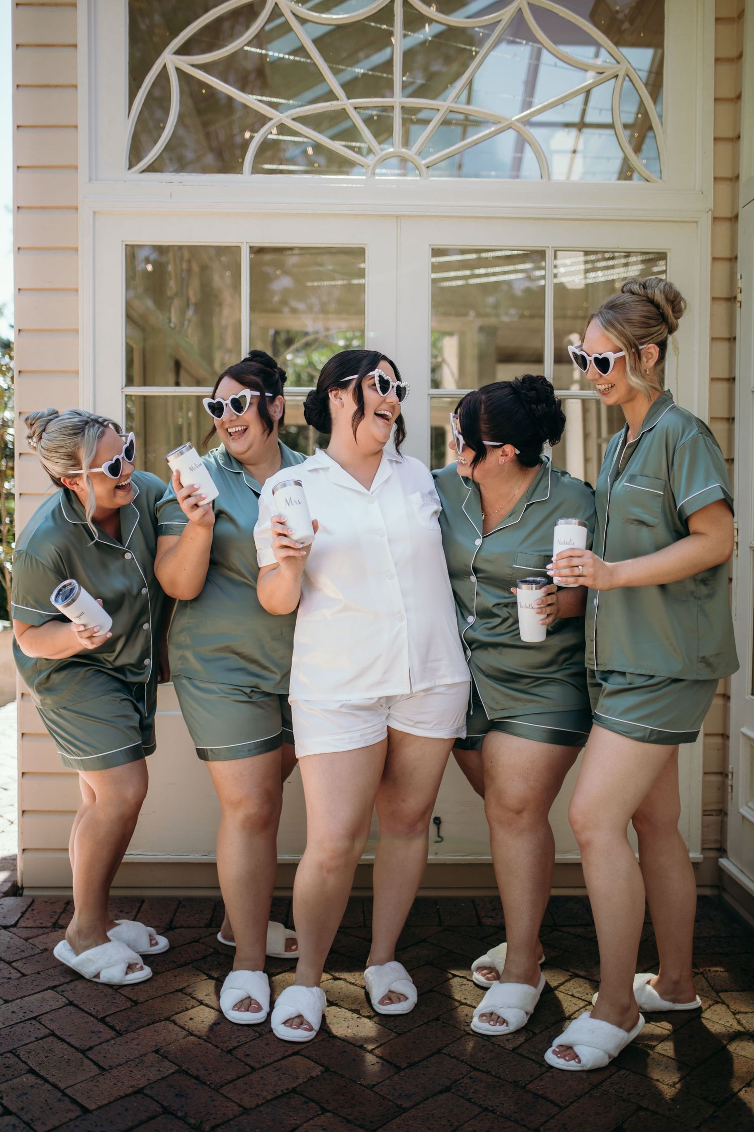 Wedding party in matching outfits poses playfully with coffee cups on a porch.