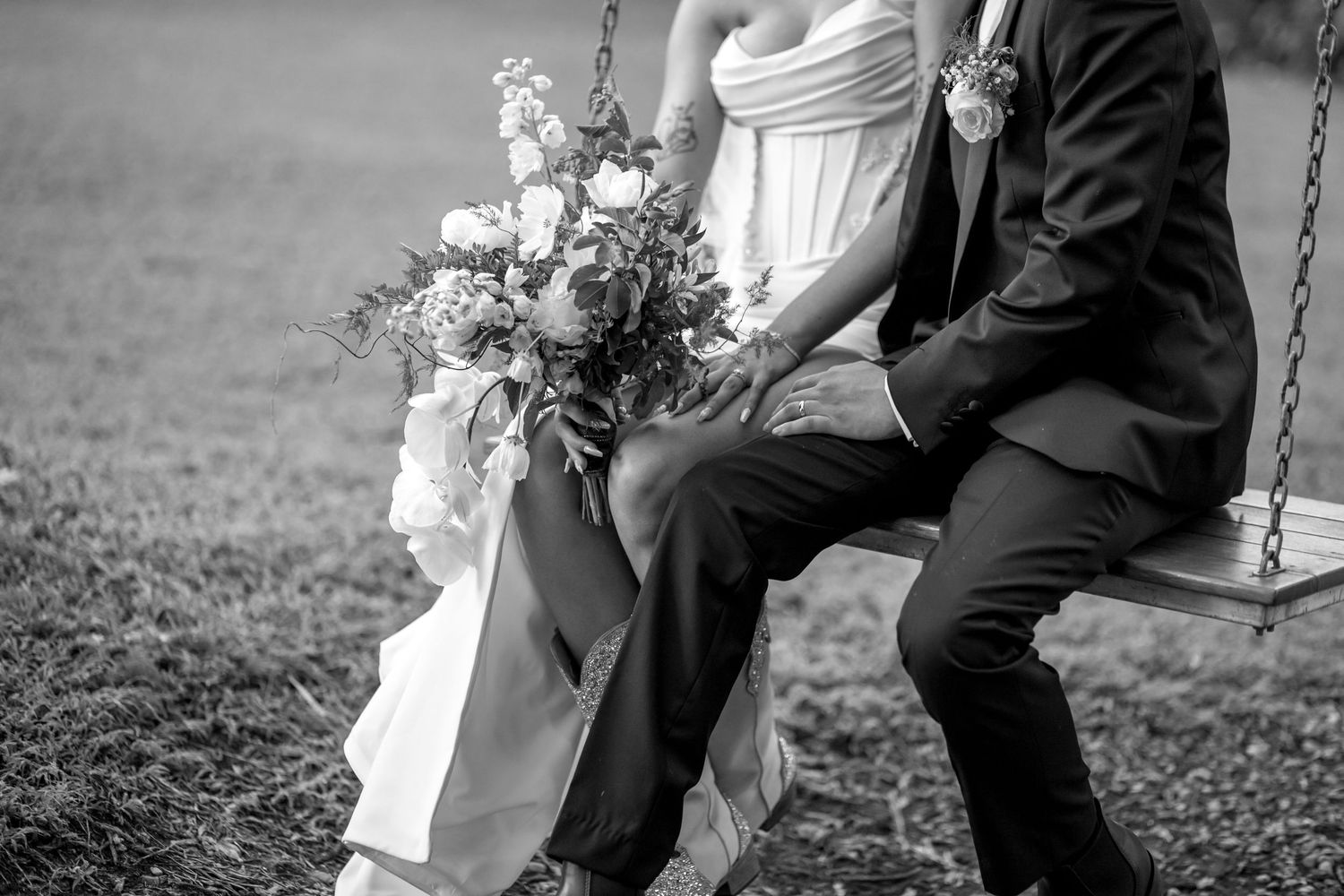 A couple in wedding attire sits together on a rustic wooden swing in a romantic outdoor setting.