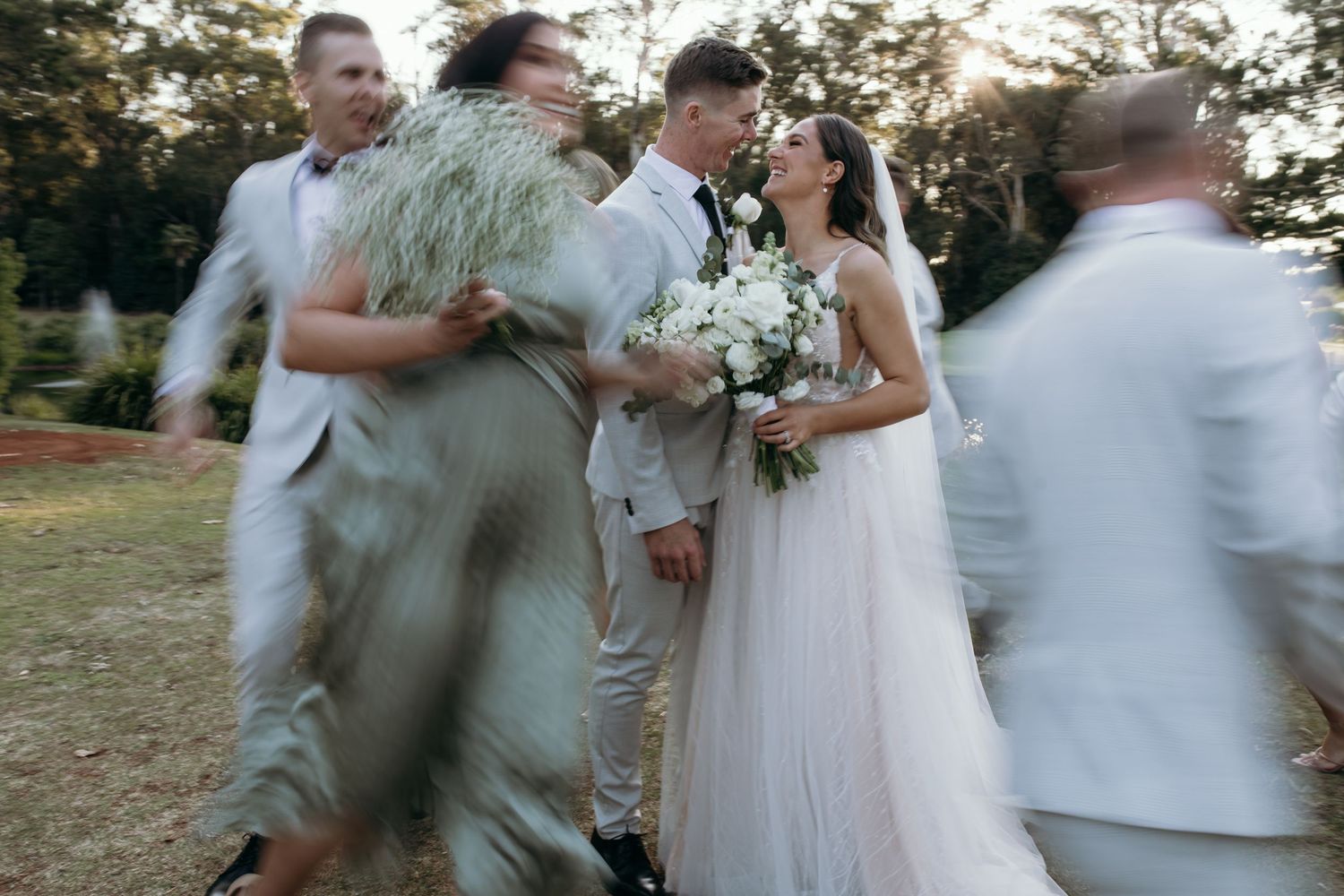 Wedding party celebrates with laughter and joy in an outdoor garden setting.