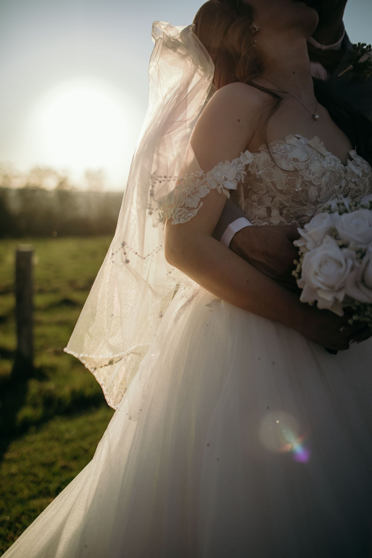 Close-up details of bride's white wedding gown and bouquet in sunset light.