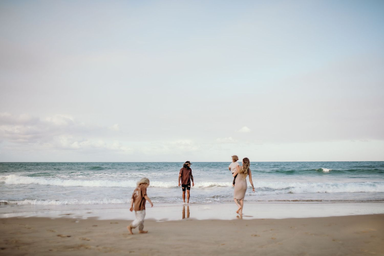 Footprints in the sand lead towards people walking along a peaceful beach at sunset.