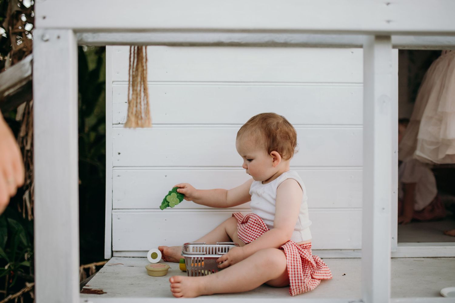 A small figure in pink clothing playing near white wooden structures outdoors.
