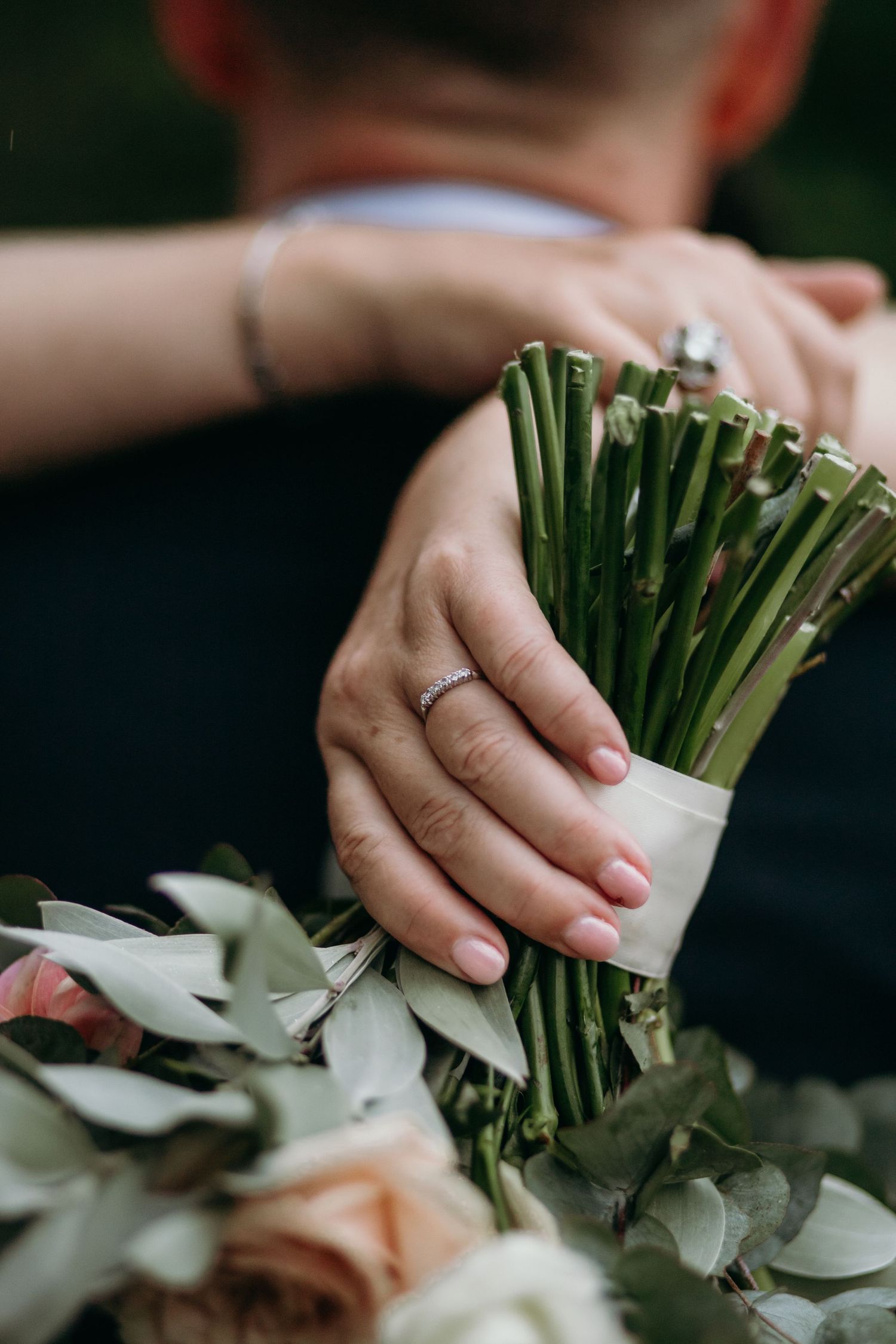 Close-up of hands holding a white and green floral wedding bouquet with ribbon wrap.