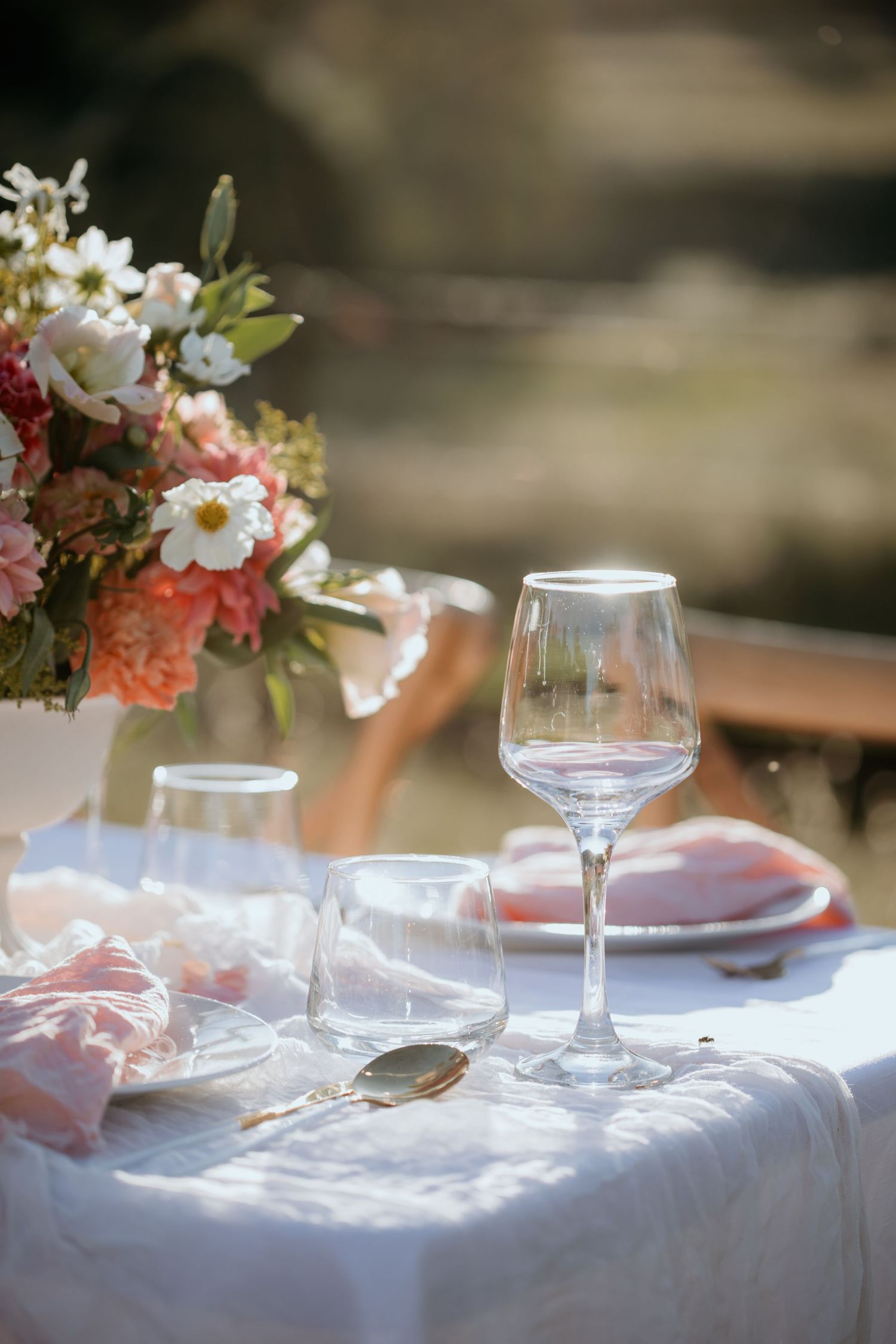Elegant table setting with wine glass and floral centerpiece on white linen tablecloth in soft natural light.