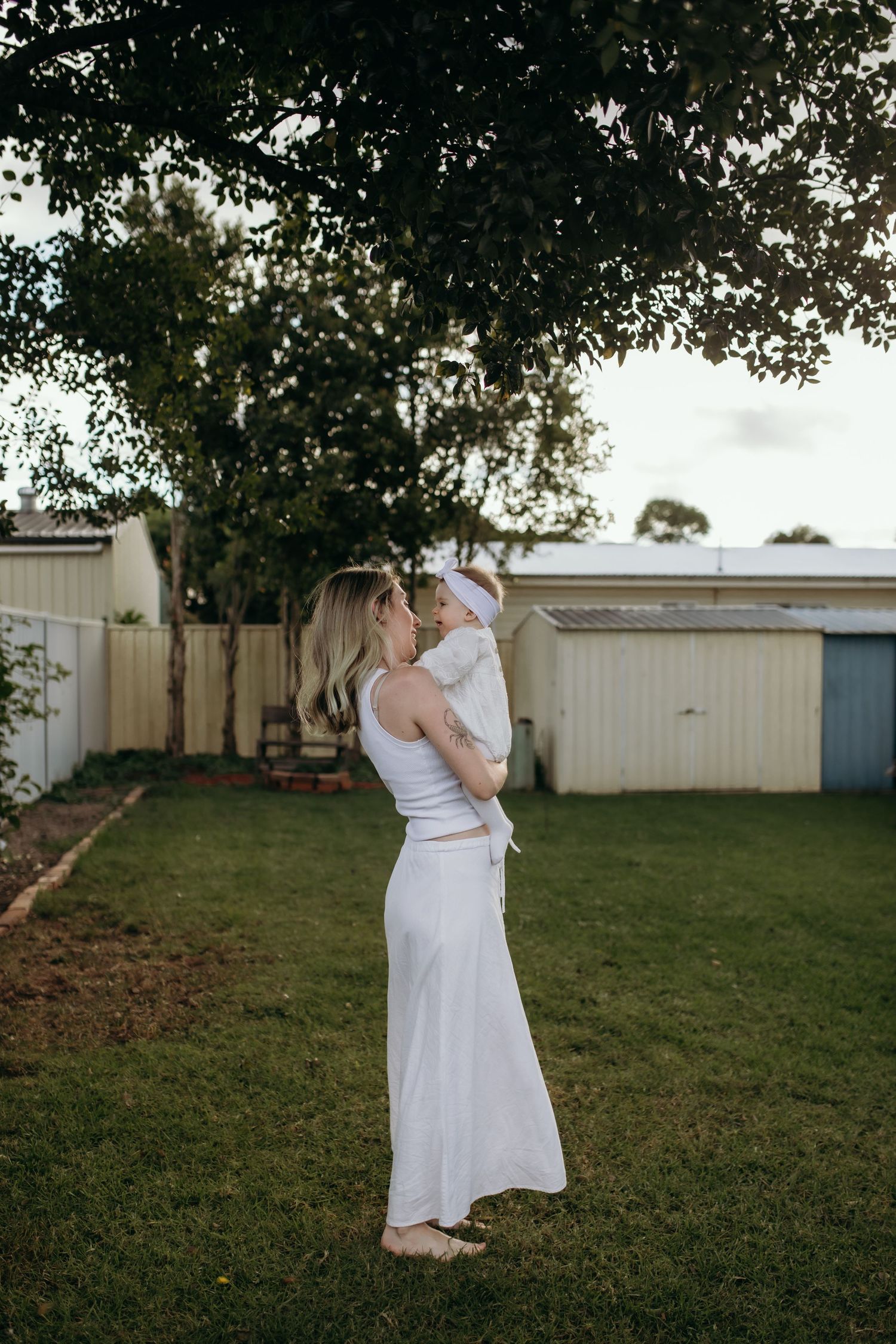 A couple in white dresses sharing a romantic moment in a backyard garden setting.