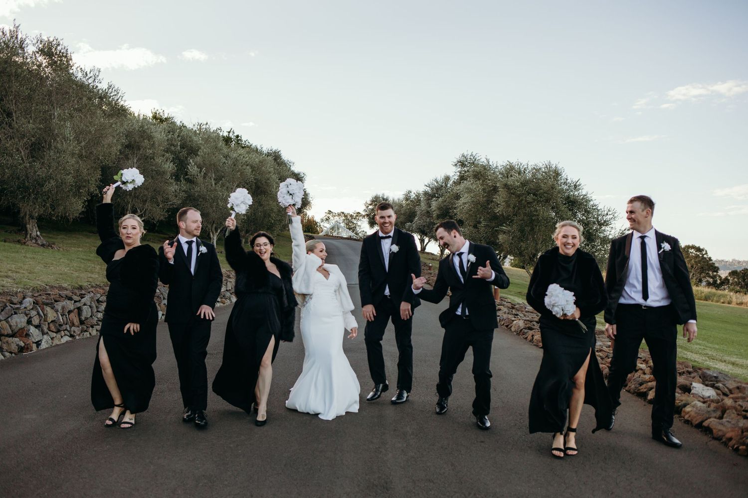 Wedding party walking together outdoors with bride in white and attendants in black formal attire.