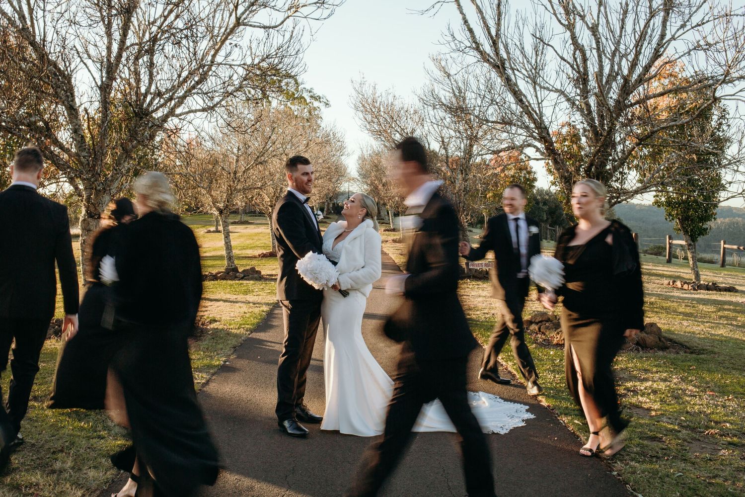 Wedding party celebrating outdoors among autumn trees at sunset.