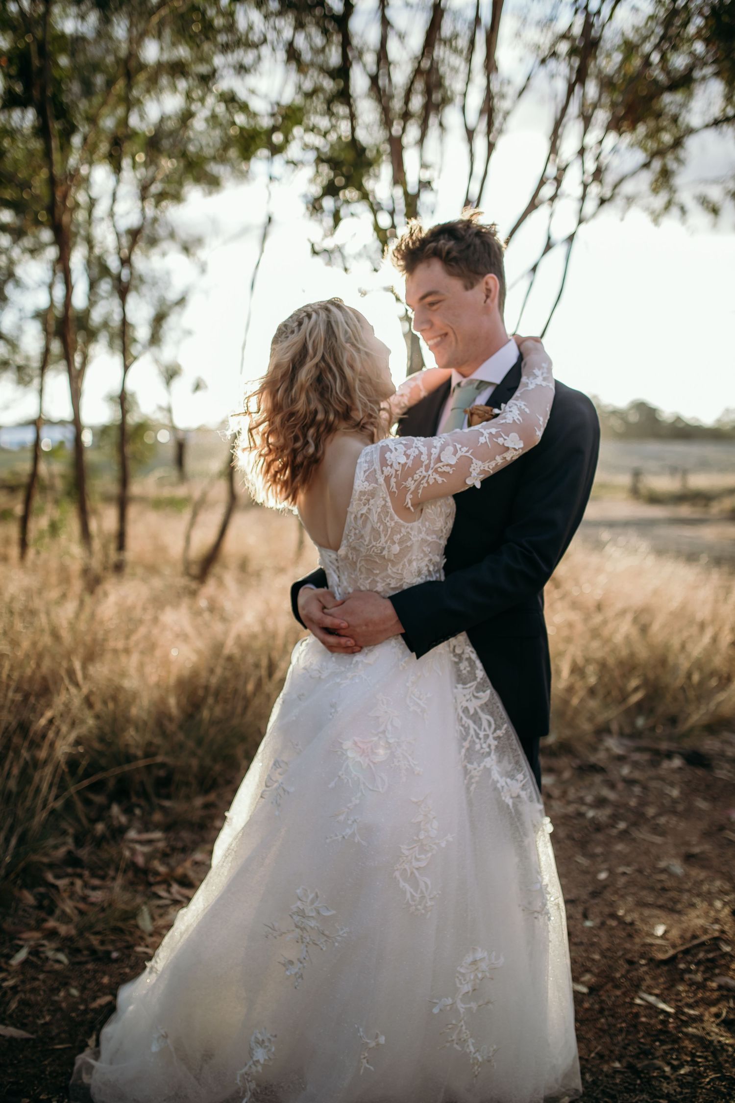 Couple dancing together in formal wedding attire among eucalyptus trees.