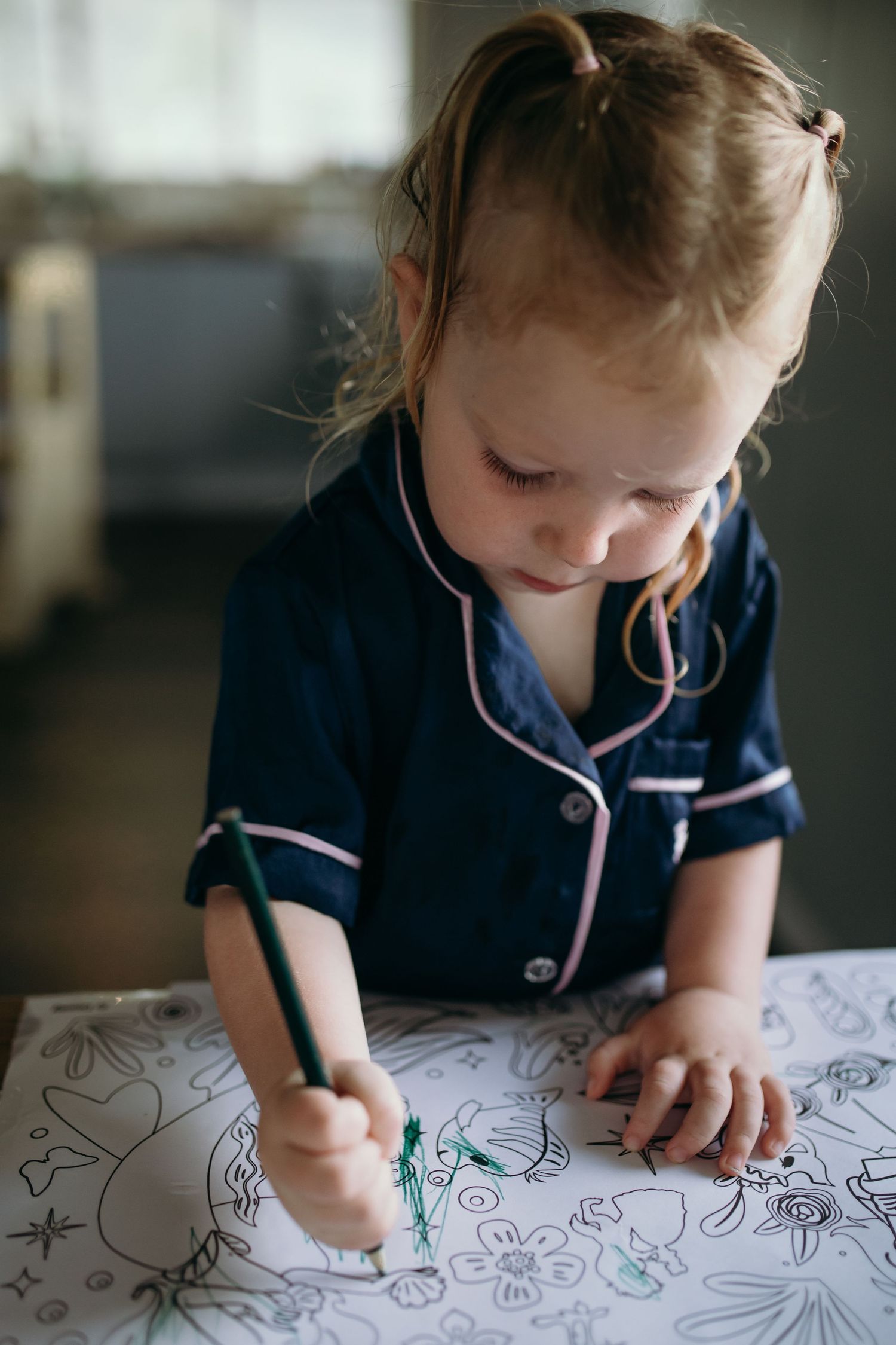 A child in navy blue pajamas coloring and drawing on paper with focused concentration.