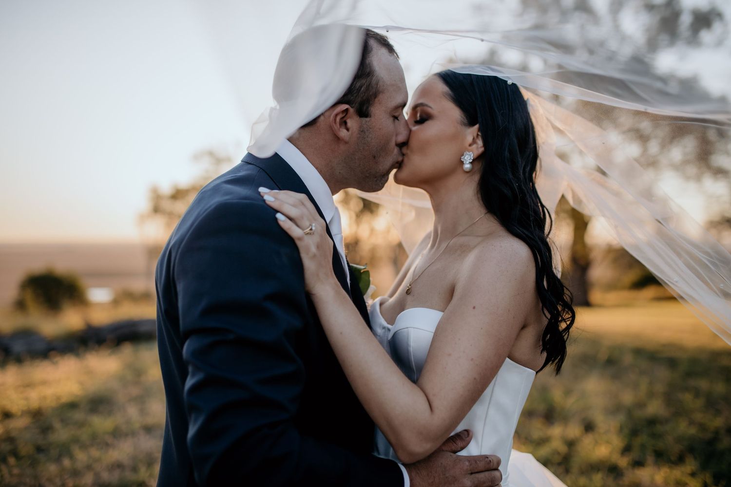 Romantic sunset wedding portrait with flowing veil in golden light.