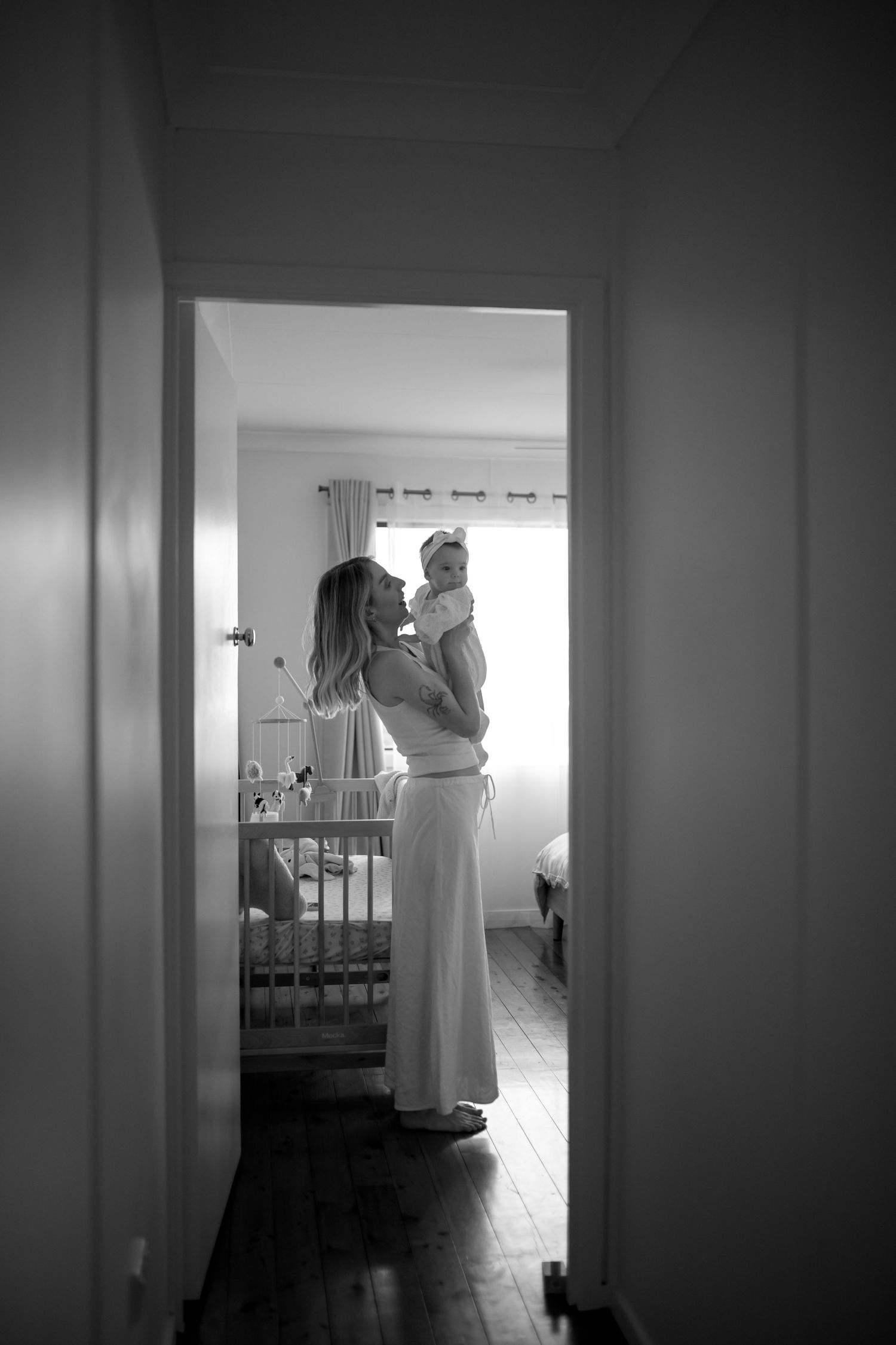 Black and white image of parent and baby standing in nursery doorway.