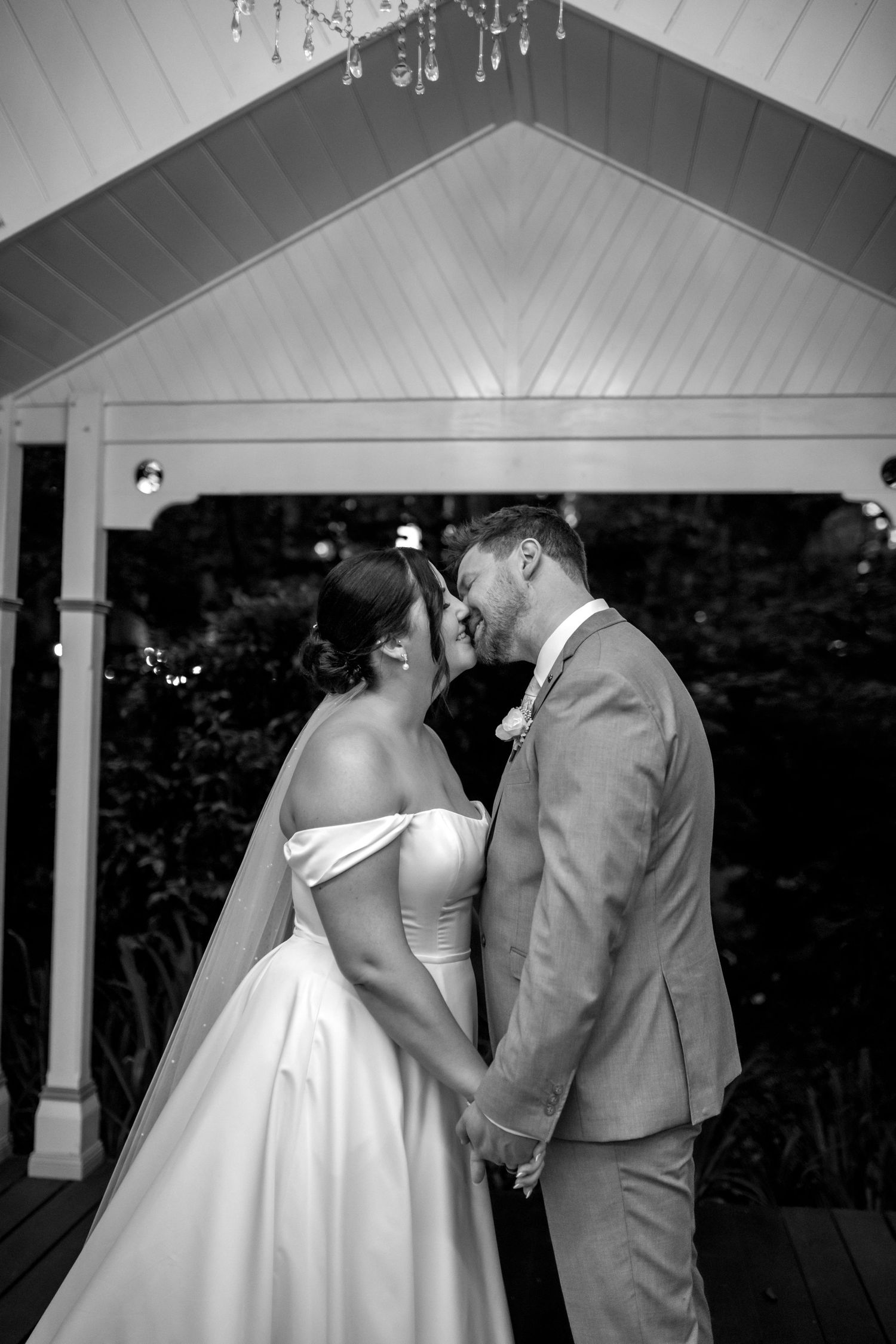 Black and white wedding portraits captured under a covered pavilion with dramatic lighting.