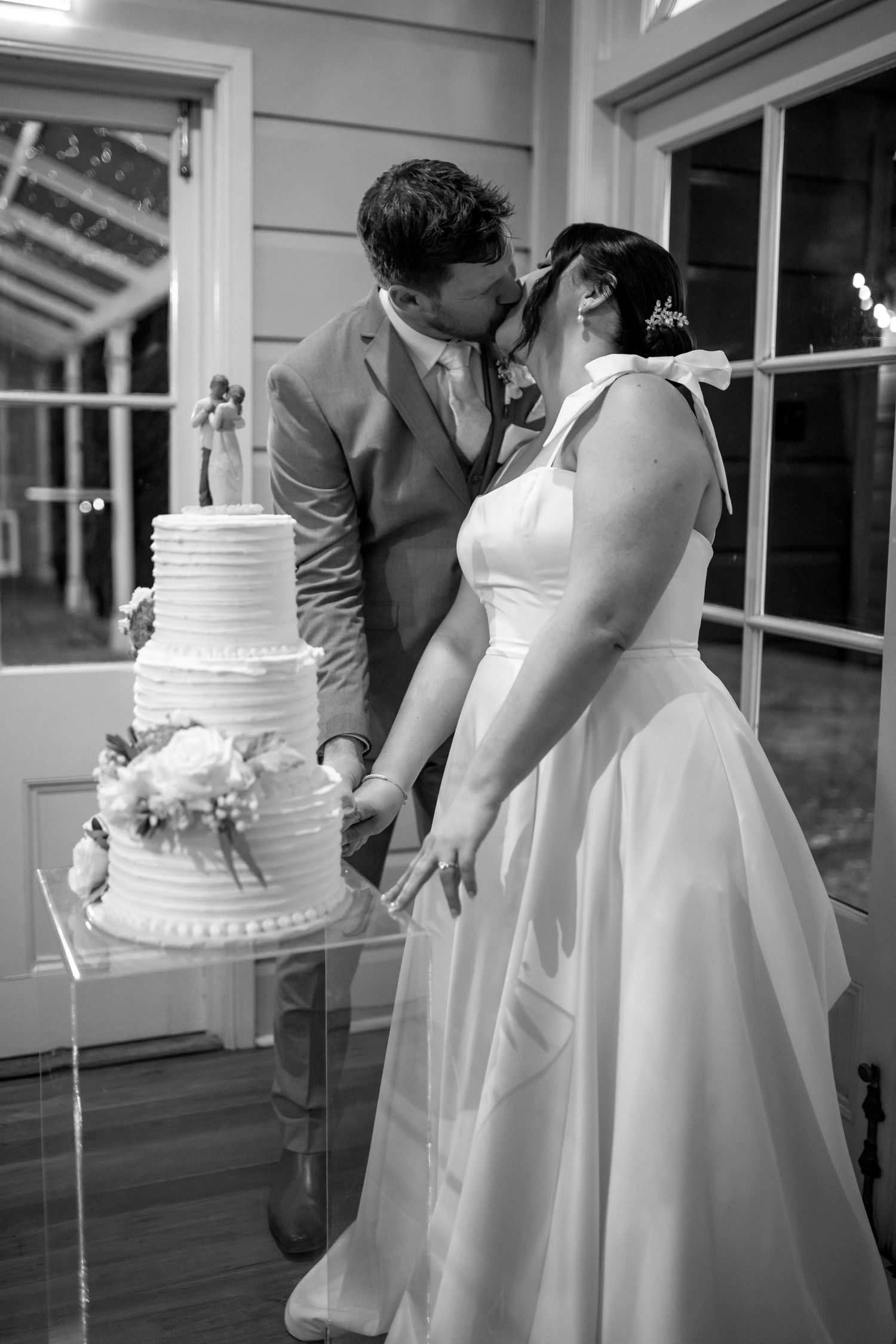 Wedding couple shares intimate moments near a white wedding cake in black and white photography.
