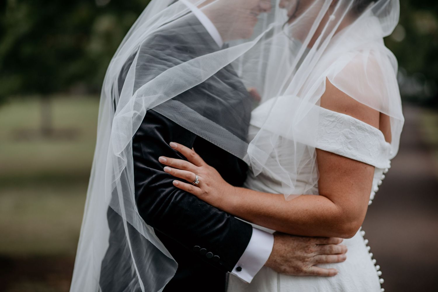 Intimate embrace captured through flowing white wedding veil.