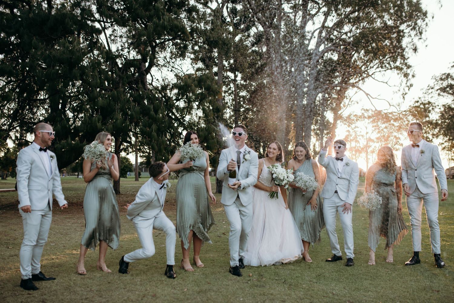 Wedding party poses together on grassy lawn during golden hour.