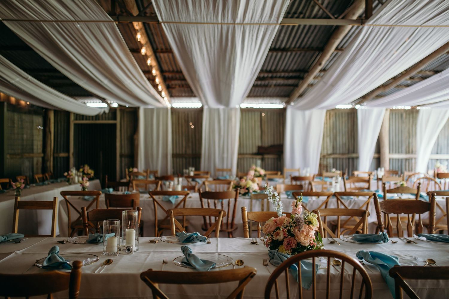 Wedding reception venue with white draped ceiling and rustic wooden chairs.