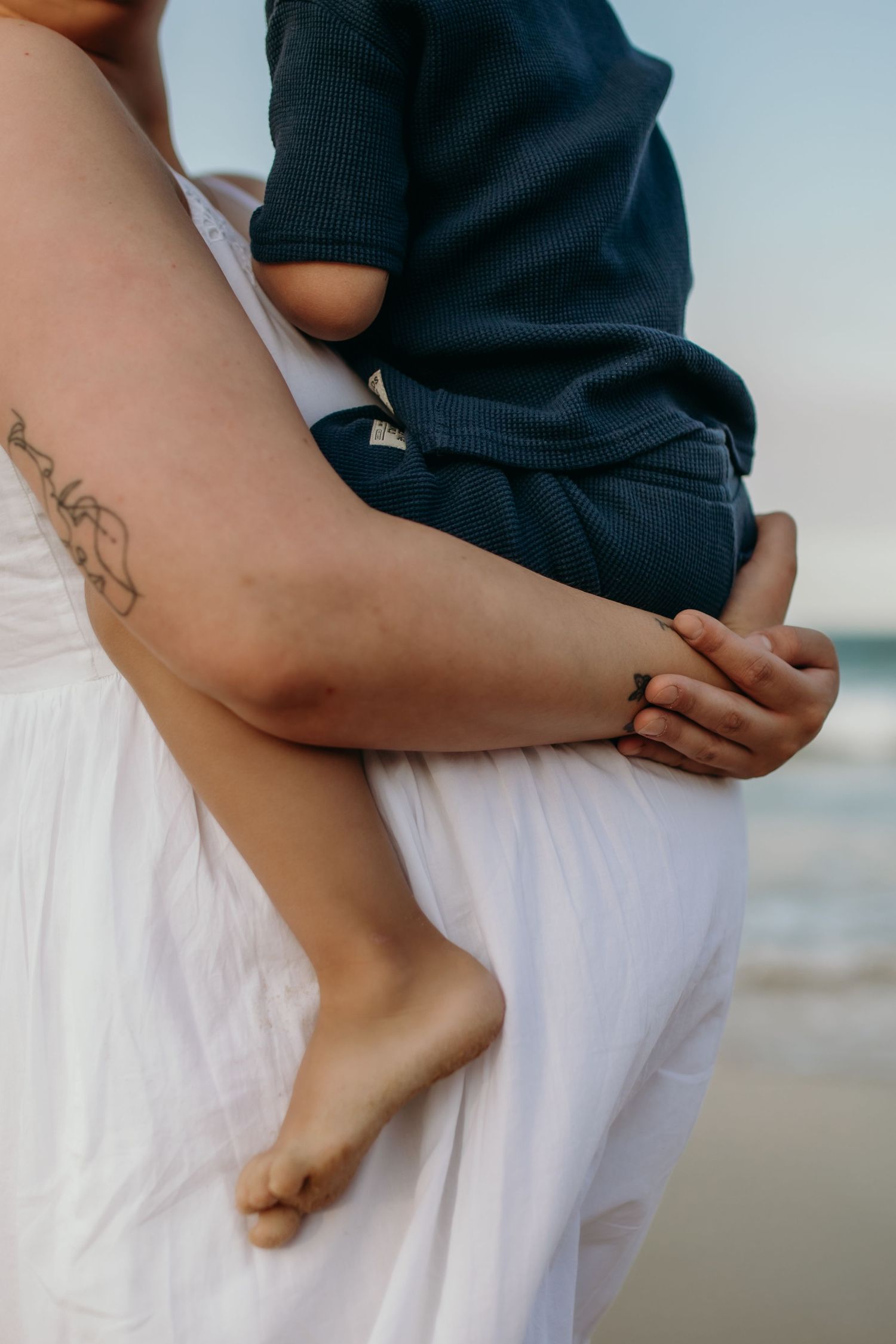 Close-up view of bare feet and casual beach attire against ocean backdrop.