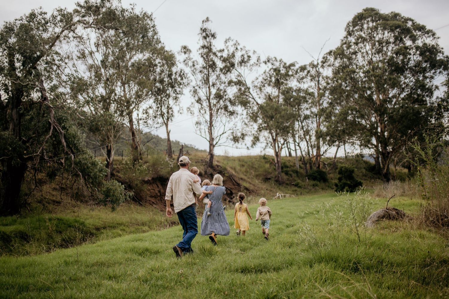 People walking through a grassy hillside with trees in the background.