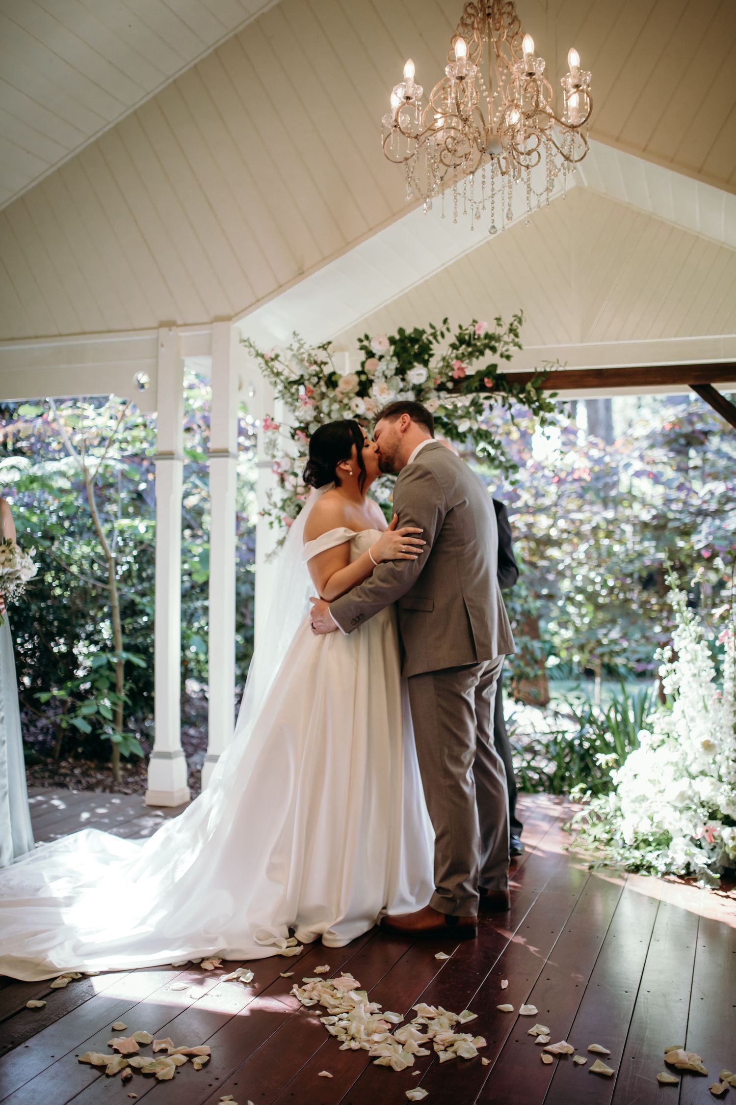 A romantic first dance moment captured under a crystal chandelier in a sunlit white pavilion.
