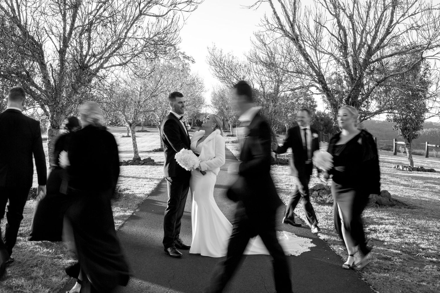 Black and white photo of wedding party having fun and dancing together outdoors.