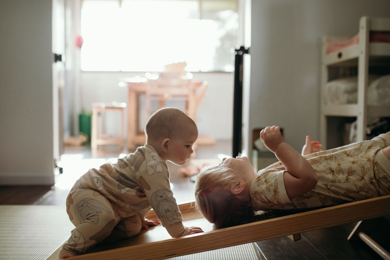 Babies lying on a wooden surface in natural window light.