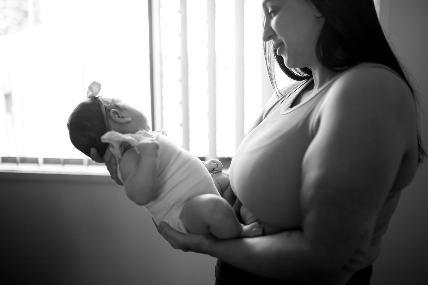 Black and white portrait of parent cradling newborn by window.