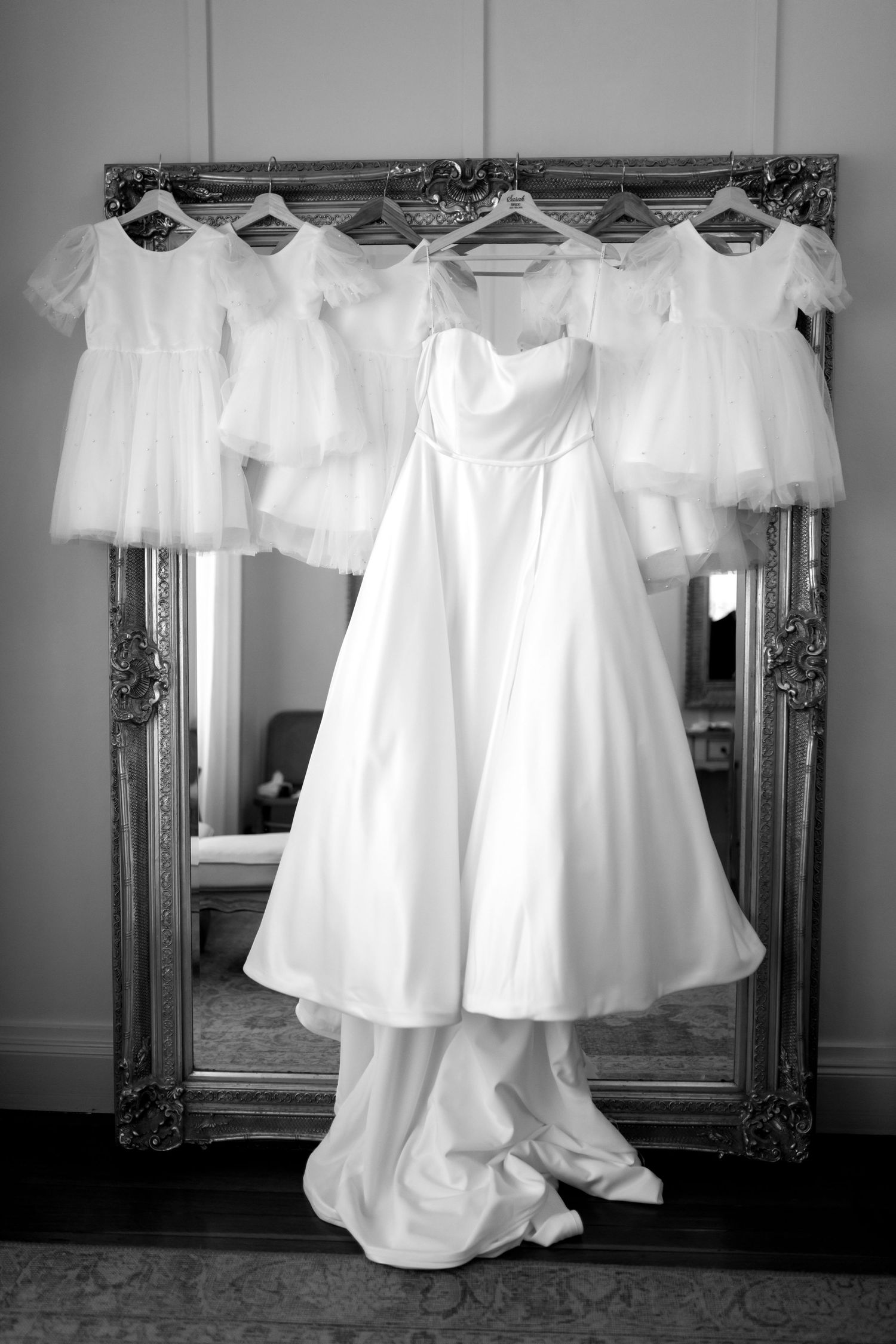 White wedding dresses and gowns hanging in a row against an ornate mirror.