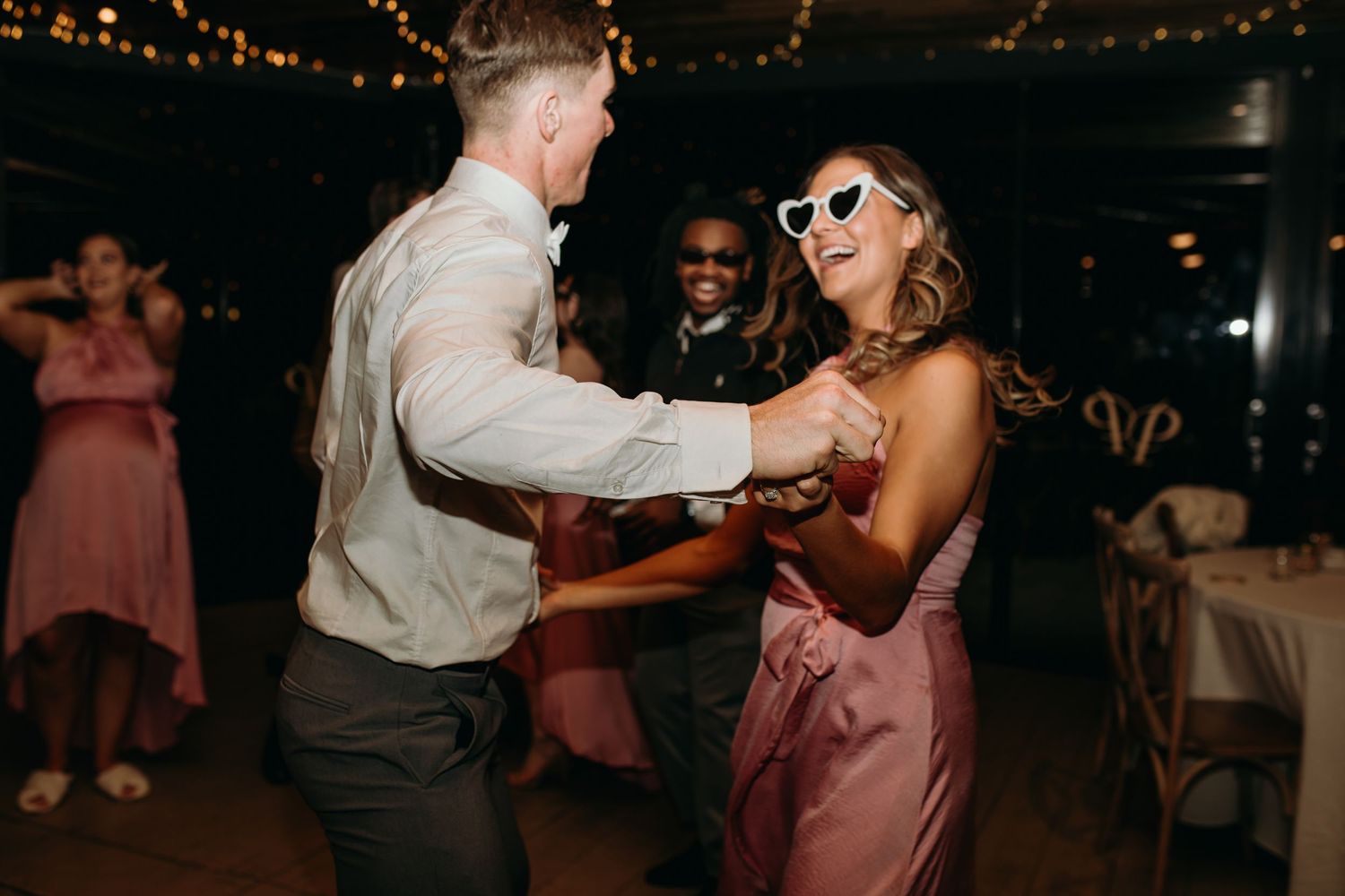 Wedding guests dance energetically at reception under dim lighting.