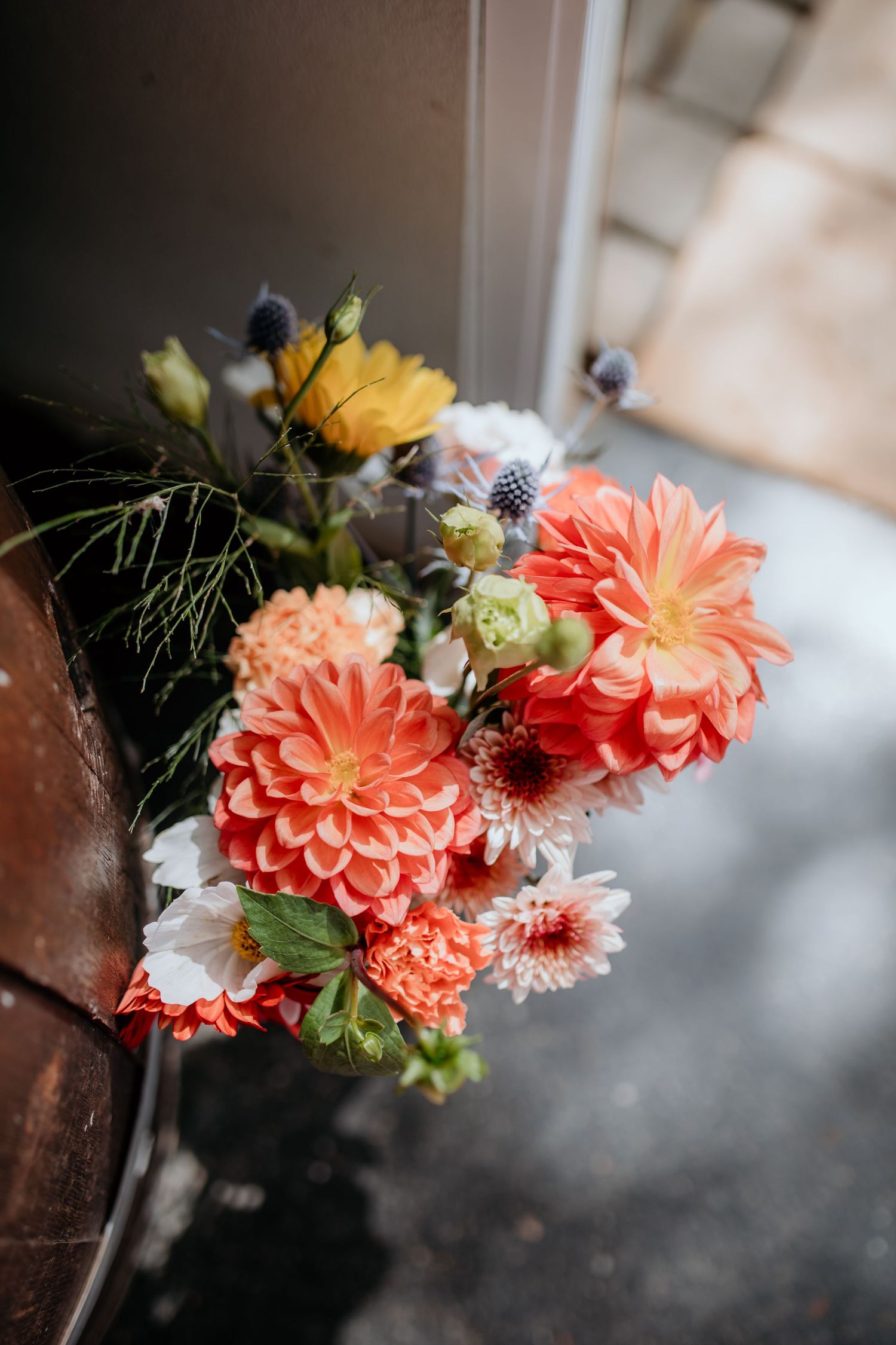 Vibrant coral dahlias and mixed flowers in a wedding arrangement by a door.