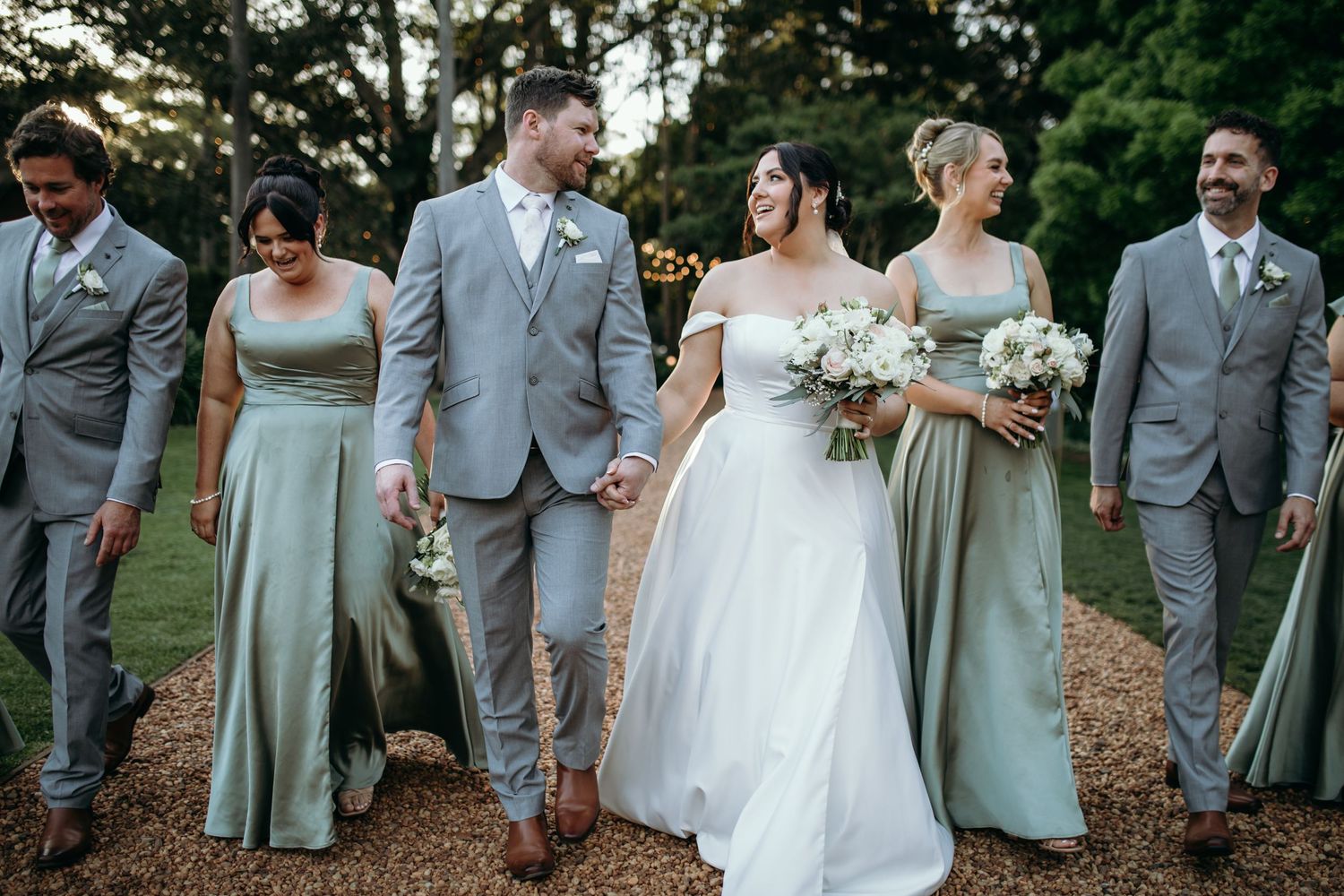 Wedding party in sage green and gray attire poses together on a tree-lined path. Gabbinbar Homestead Toowoomba.