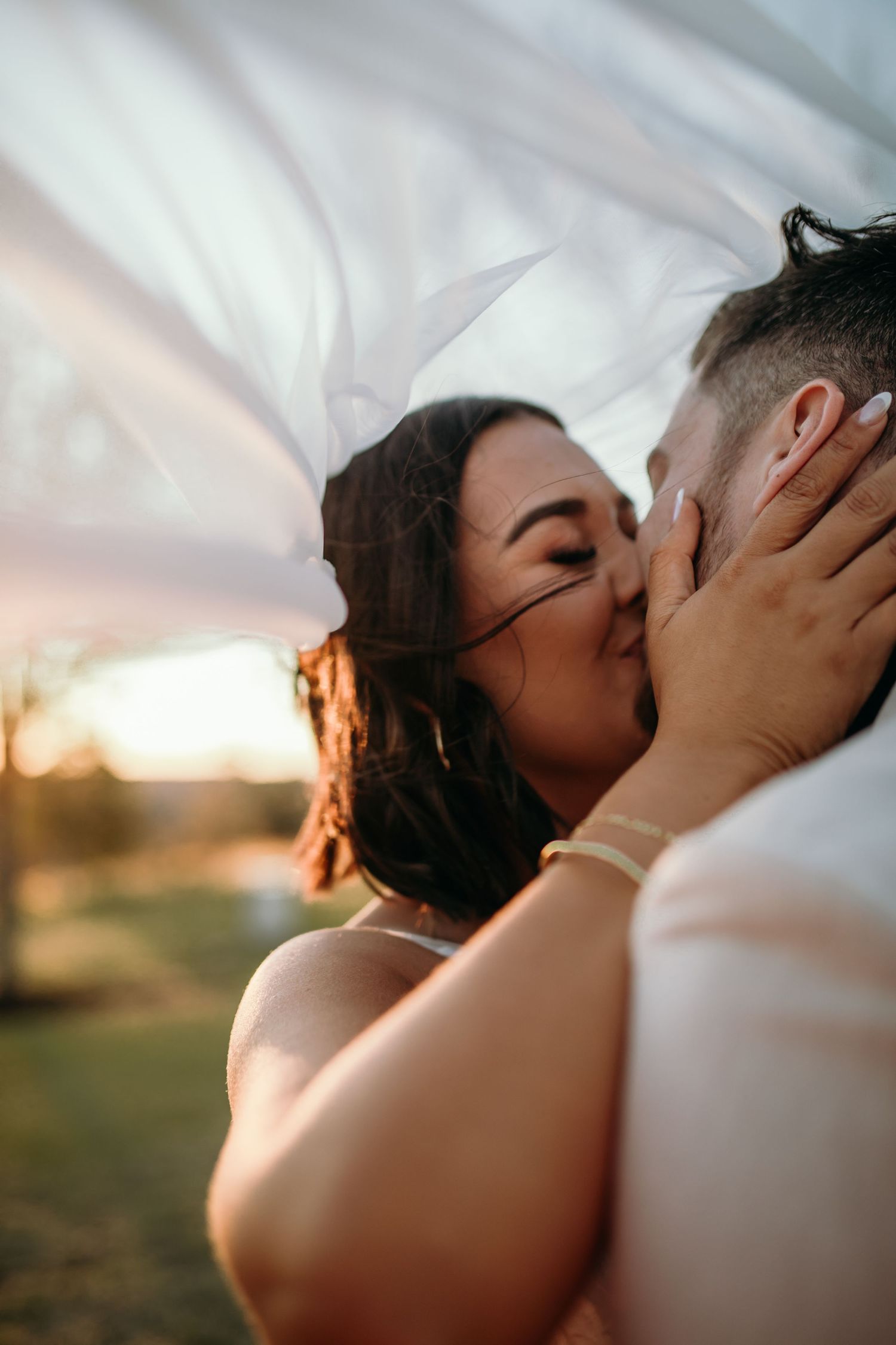 Romantic wedding couple shares an intimate kiss under flowing white veil.